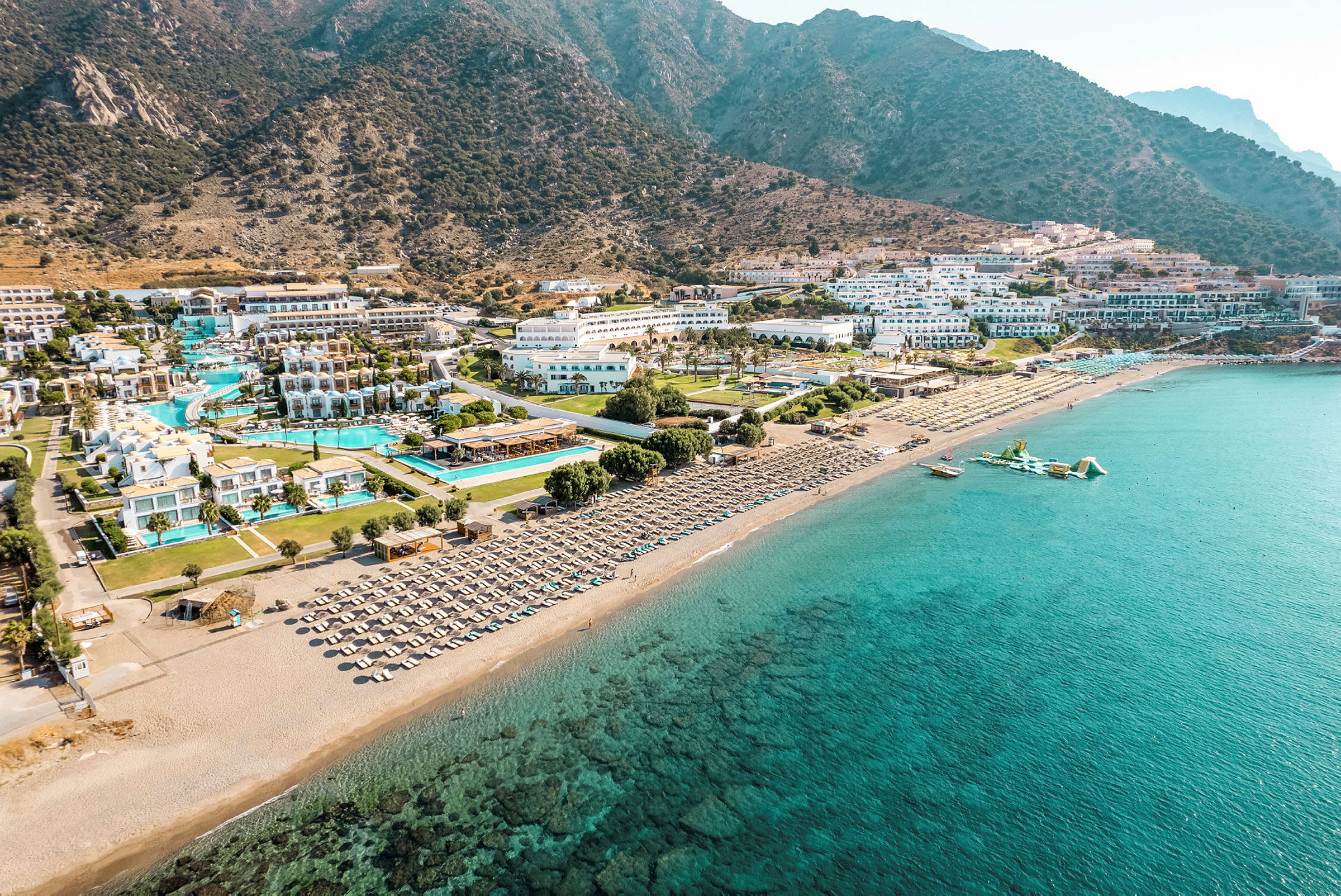 Flygfoto av en kustlinje med hotellkomplex vid stranden, pooler och solstolar. (AI-genererad text)