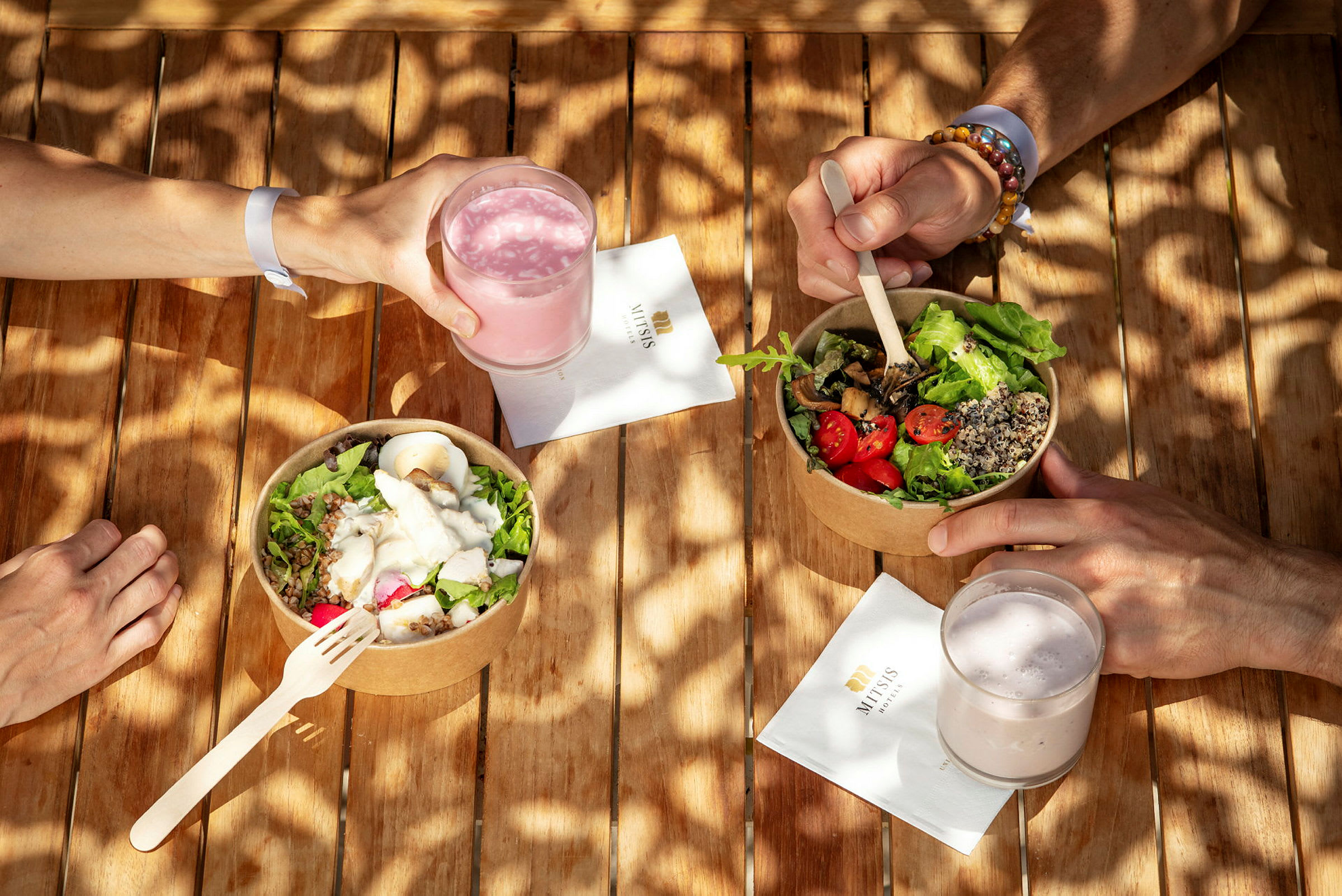 En hand håller ett glas rosa dryck bredvid två skålar med sallad. (AI-genererad text)