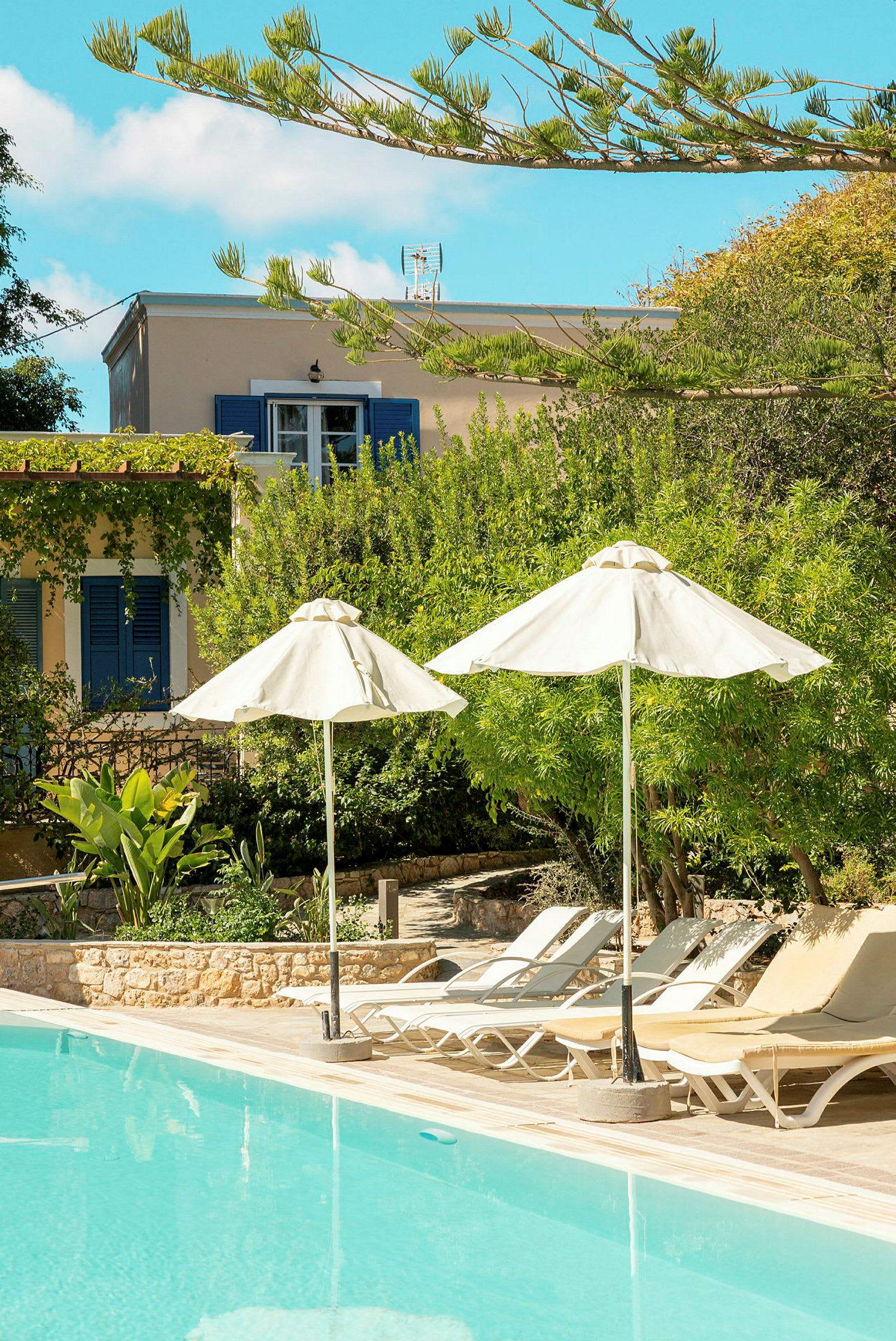 Poolområde med solstolar, parasoller och grönska. I bakgrunden syns ett hus. (AI-genererad text)