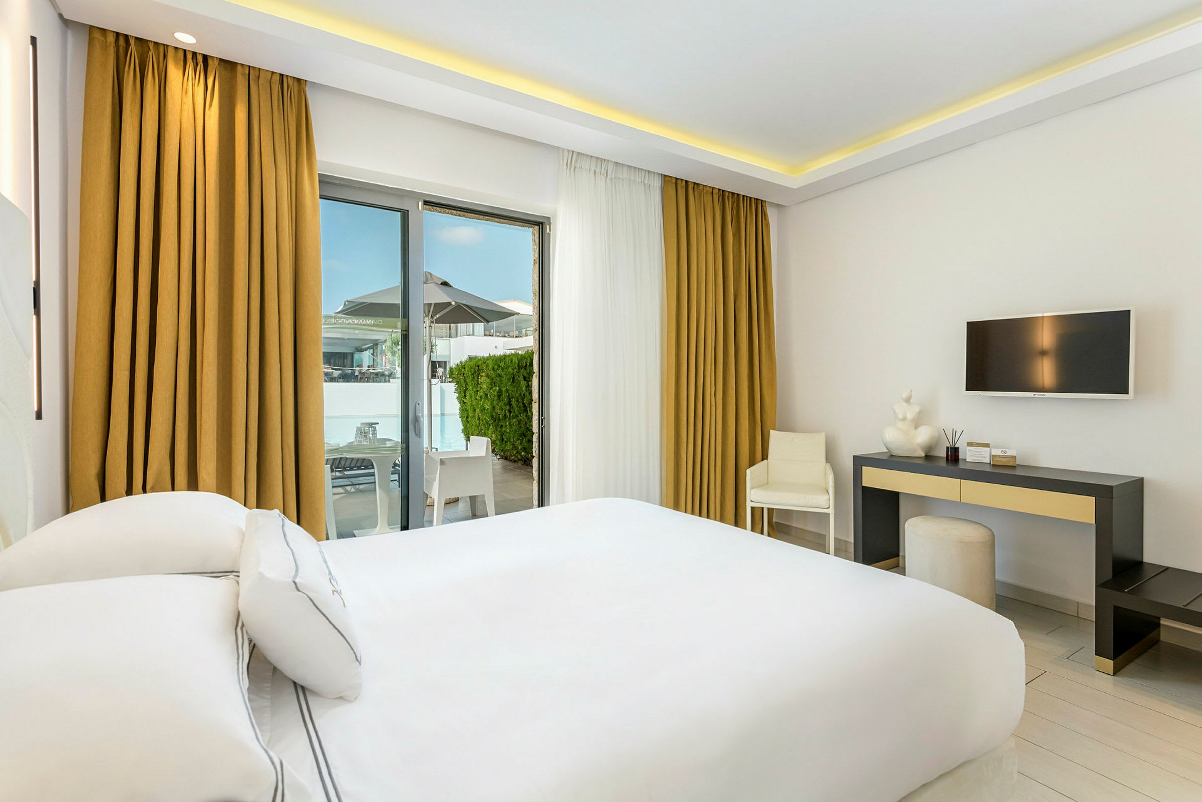 Hotelrum med vit inredning, en dubbelsäng, skrivbord och utgång till terrass. (AI-genererad text)