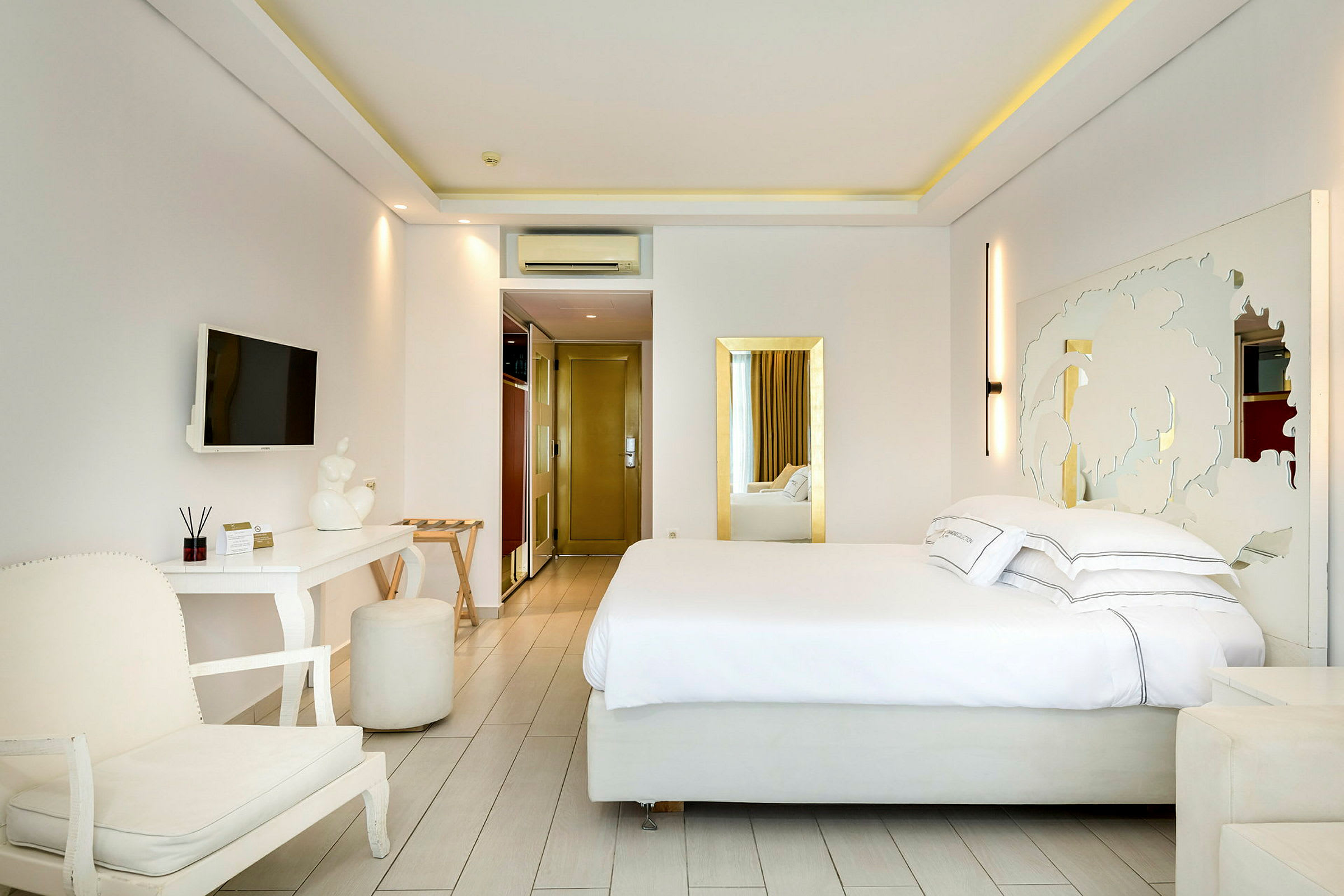 Ett hotellrum med en stor säng, vita möbler och dekorativ spegel. (AI-genererad text)