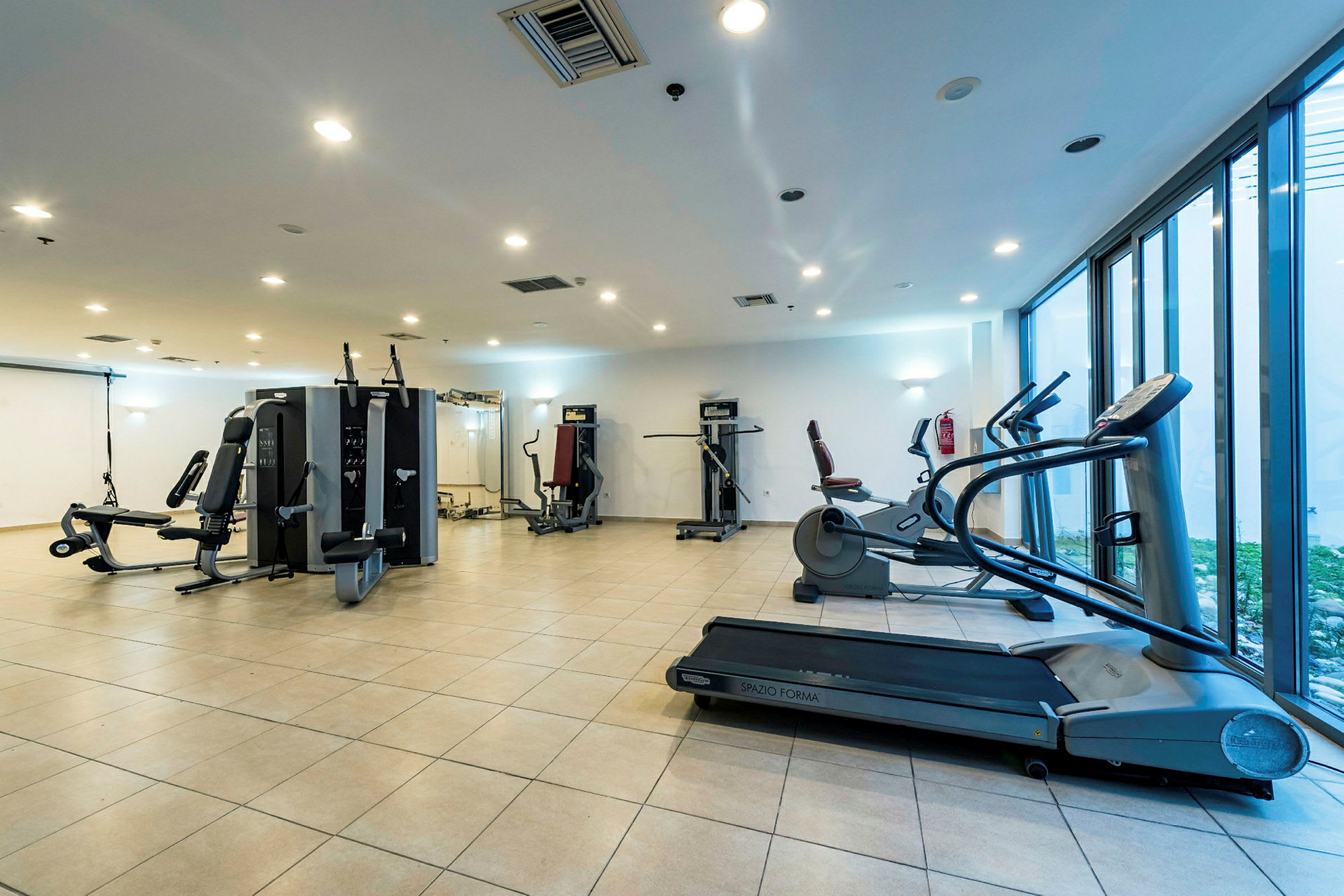 Ett gym med olika träningsmaskiner och fönster mot utsidan. (AI-genererad text)