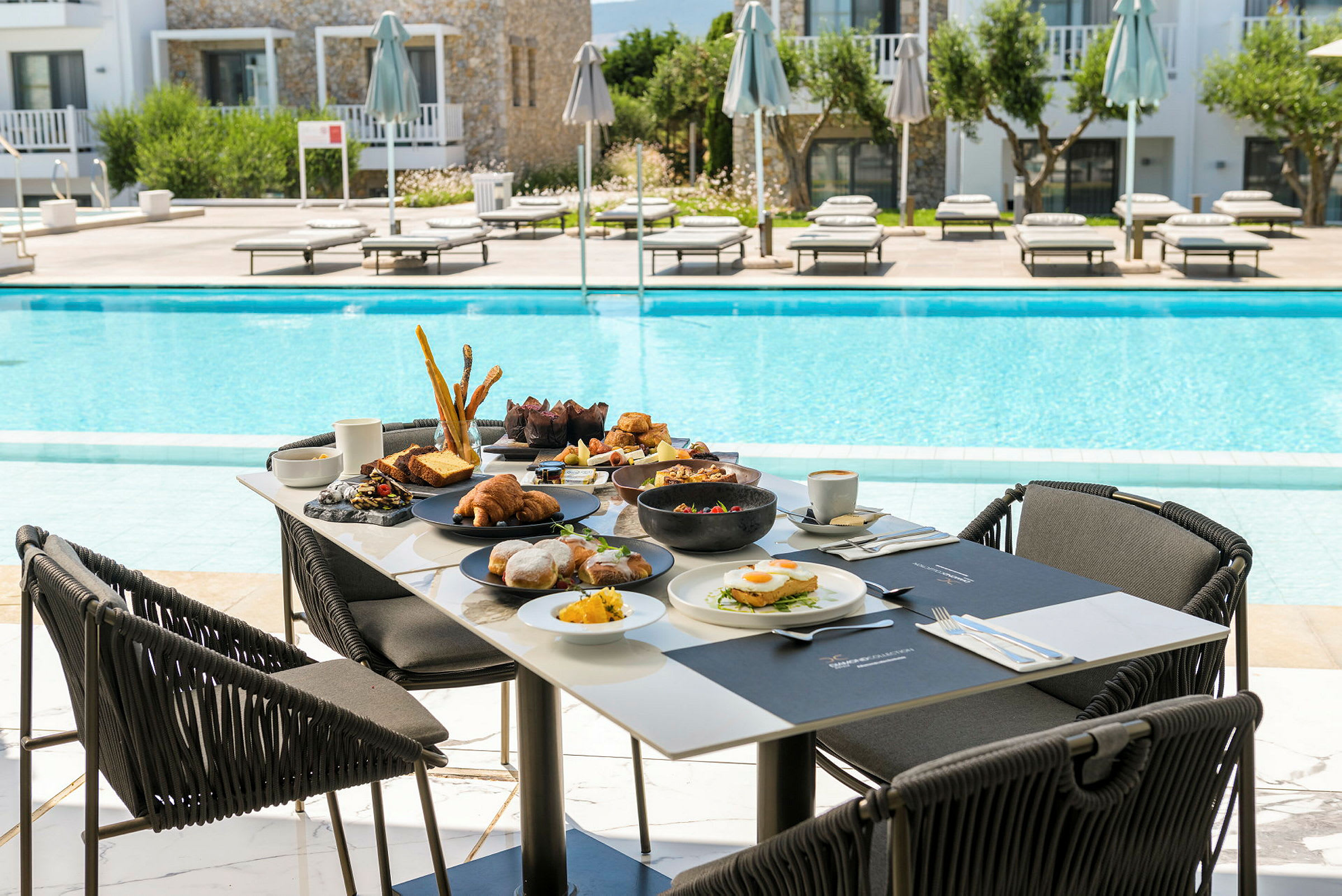 Frukostbord vid en pool med en resort i bakgrunden. (AI-genererad text)