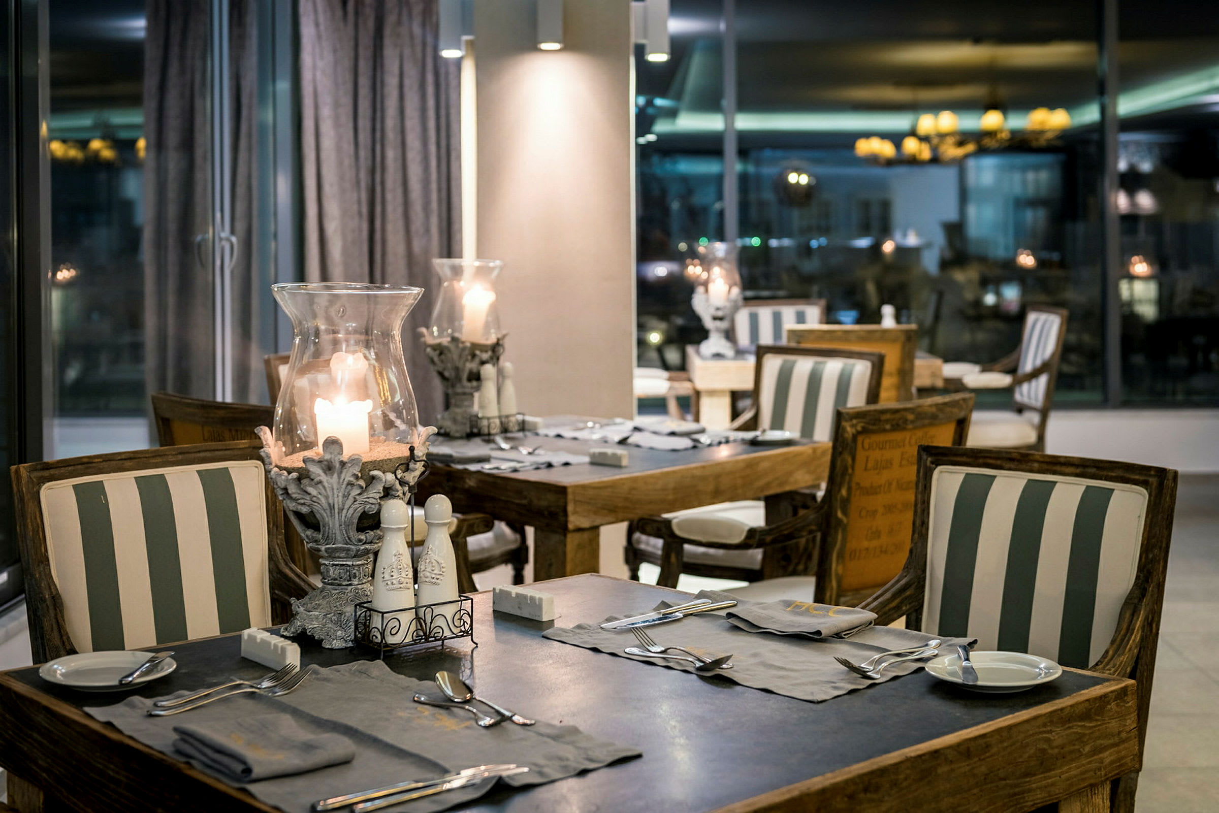 En restaurang med bord och stolar dekorerade med randiga kuddar och tända ljus. (AI-genererad text)