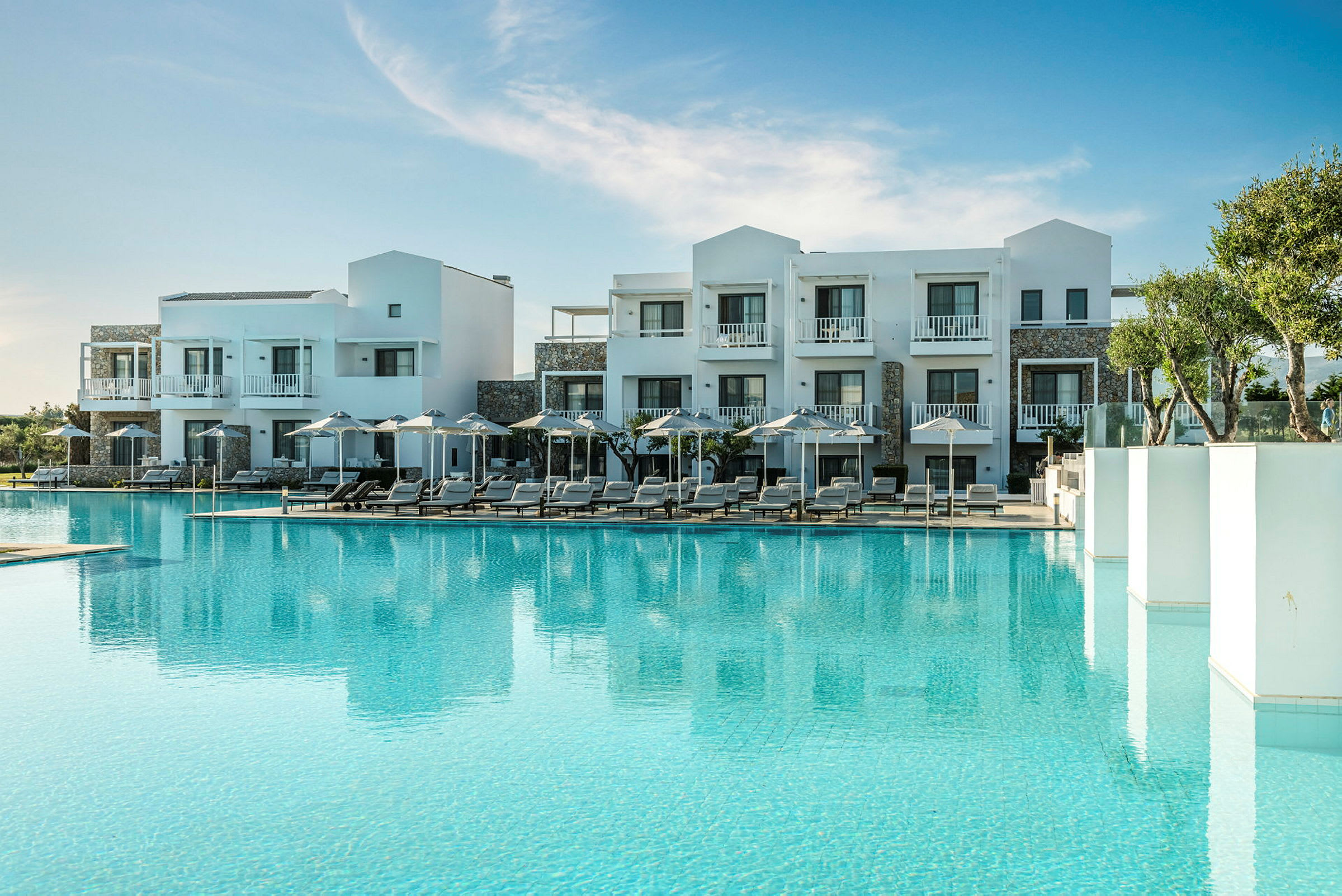 Hotellbyggnad med pool och solstolar i skärgårdsmiljö. (AI-genererad text)