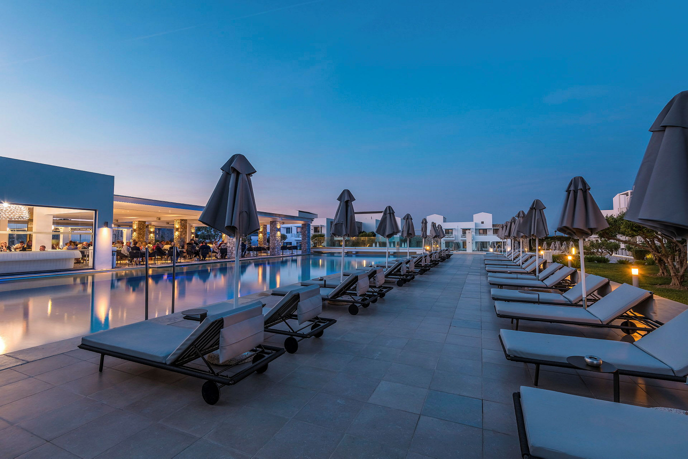 En hotellpool med solstolar och parasoll vid skymning. (AI-genererad text)