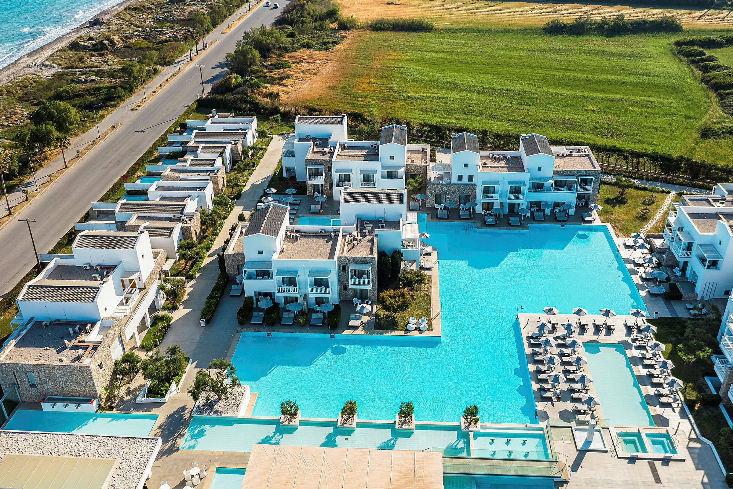 Vy över ett hotellkomplex med pooler och omgivande byggnader nära havet. (AI-genererad text)