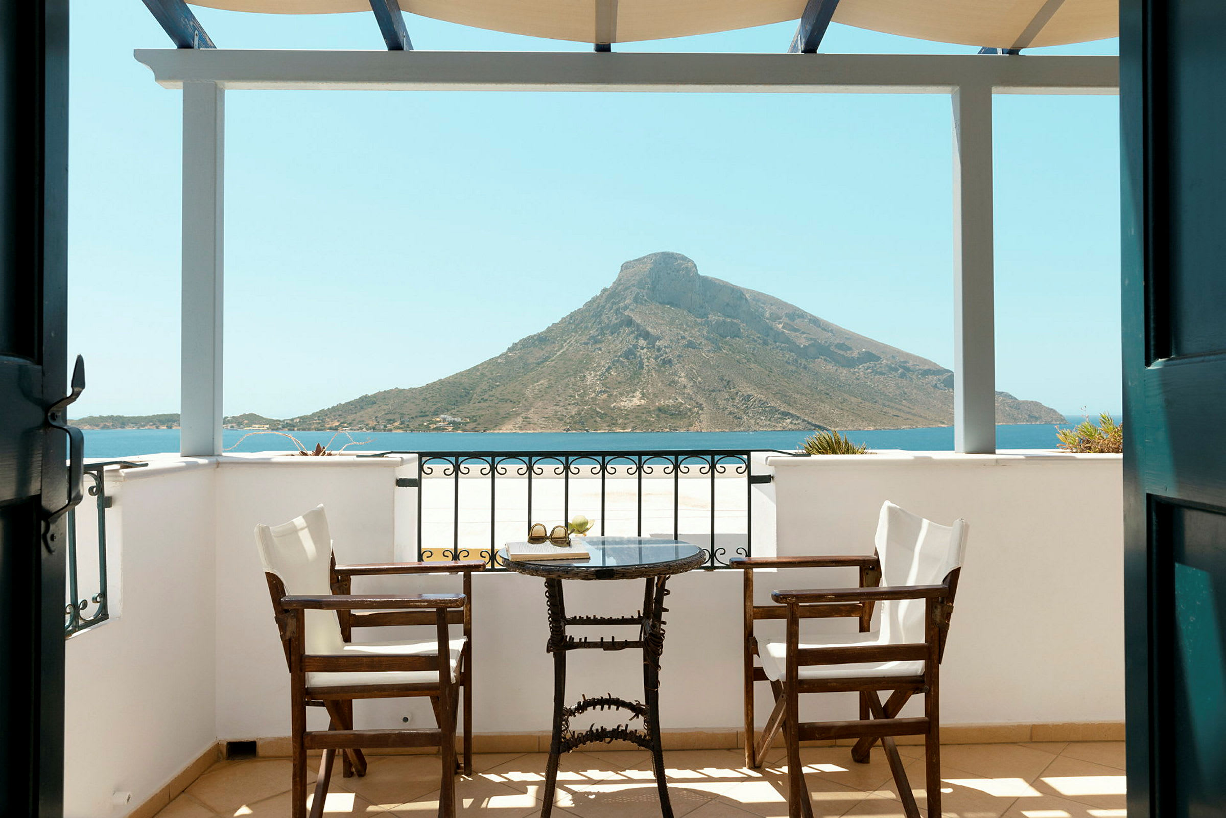 Veranda med två stolar och ett bord, utsikt mot havet och berg. (AI-genererad text)