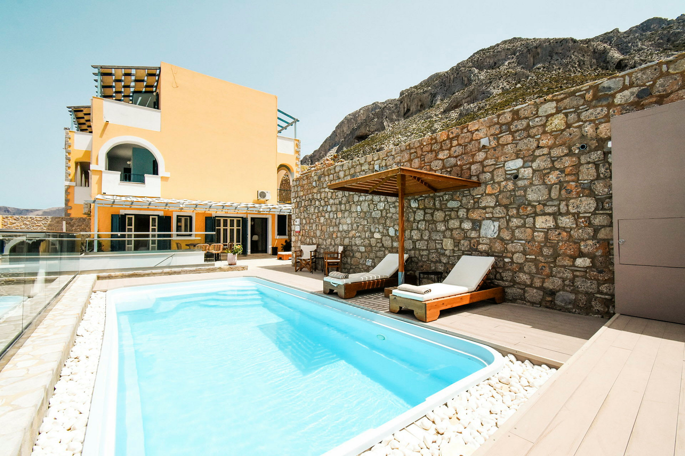 En swimmingpool framför ett gult hus och en stenmur. (AI-genererad text)