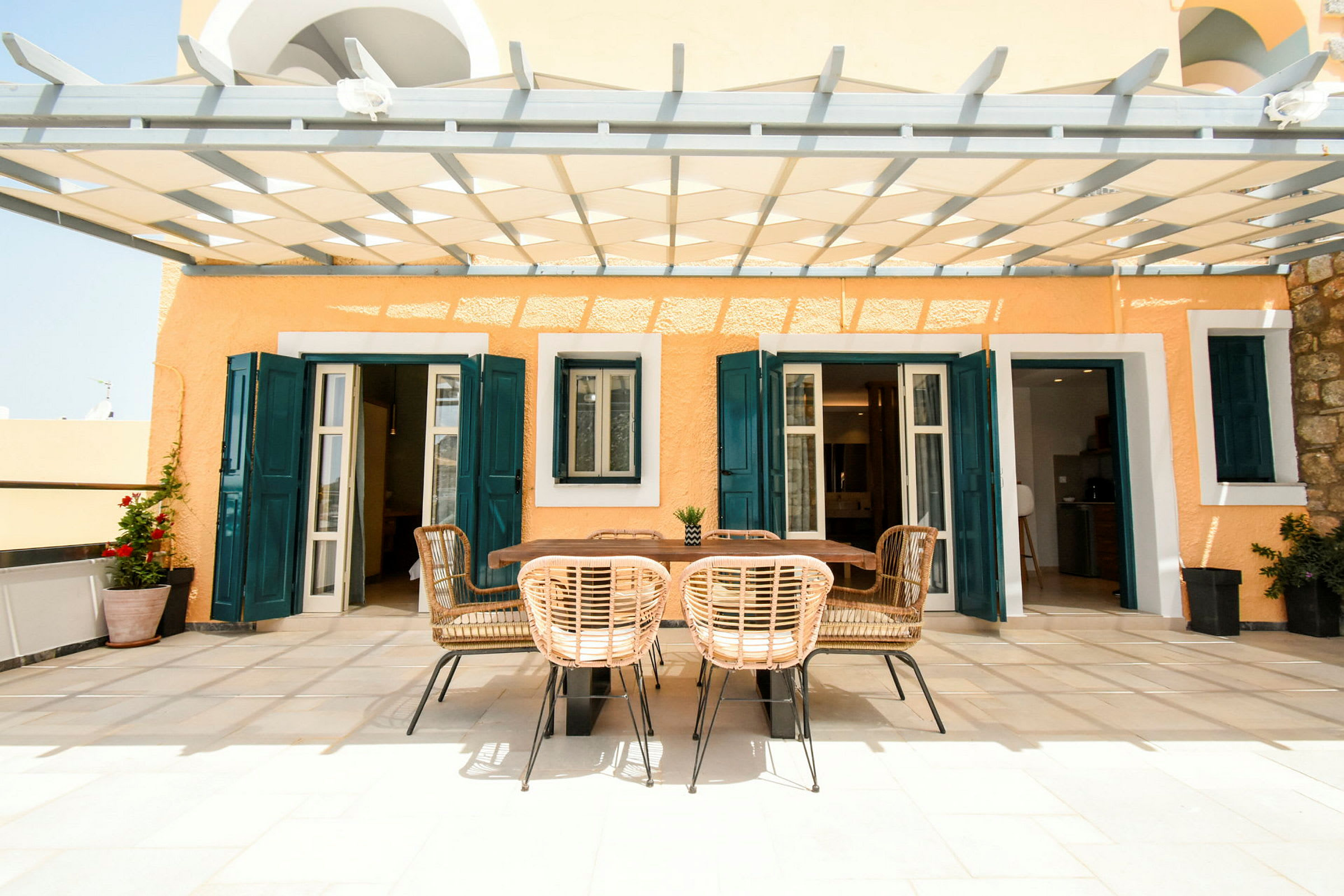 En terrass med en matplats under en pergola, omgiven av färgade husväggar. (AI-genererad text)