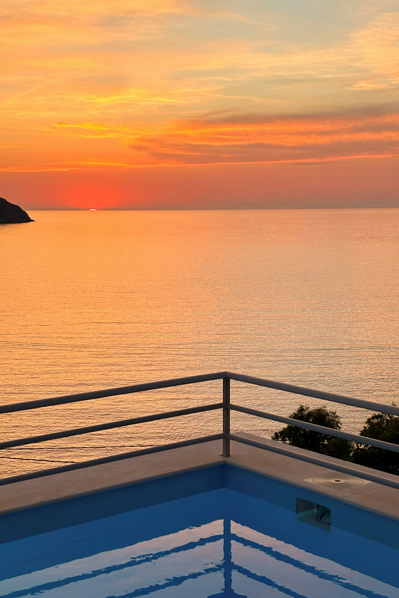 Solnedgång över havet med en pool kantad av ett räcke i förgrunden. (AI-genererad text)