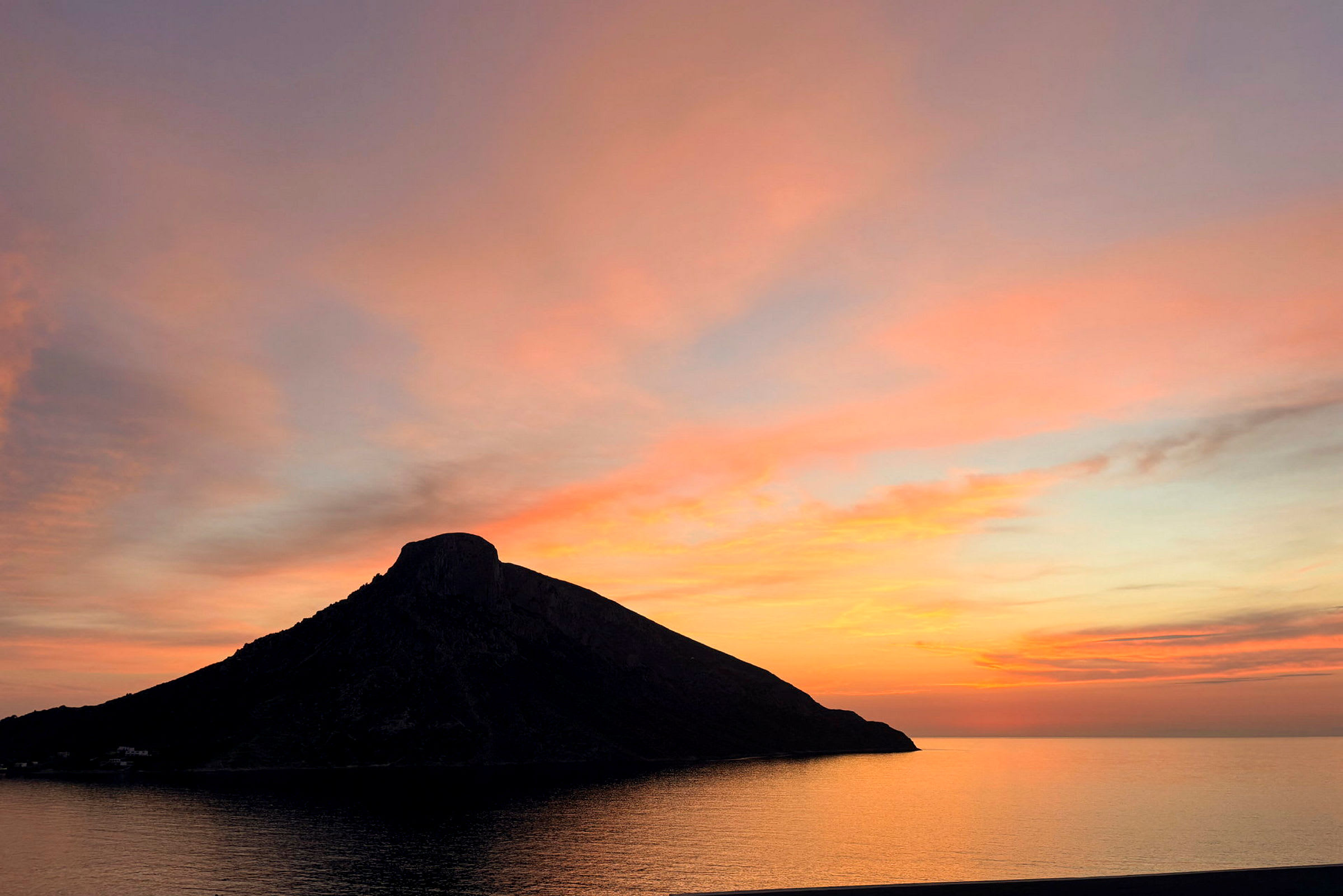 En siluett av en kulle vid havet mot en färgglad solnedgång. (AI-genererad text)