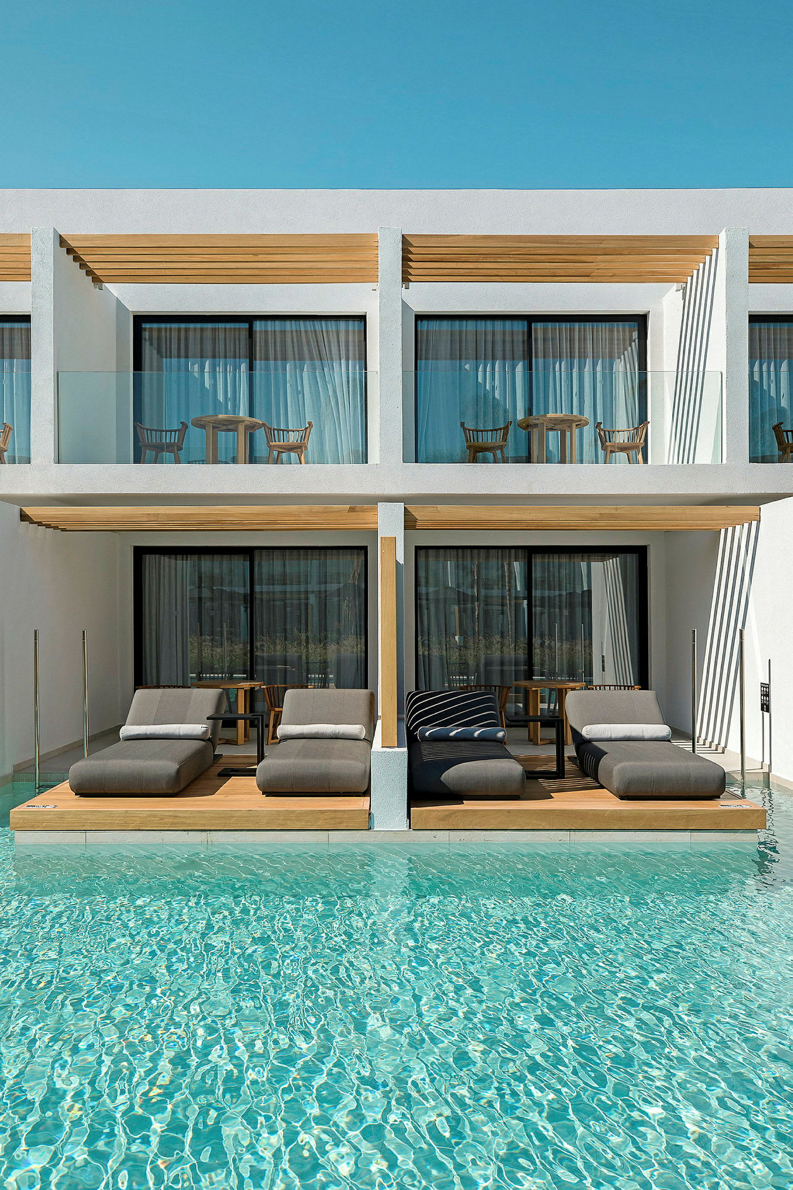 Lyxiga solsängar vid en pool framför moderna hotellrum. (AI-genererad text)