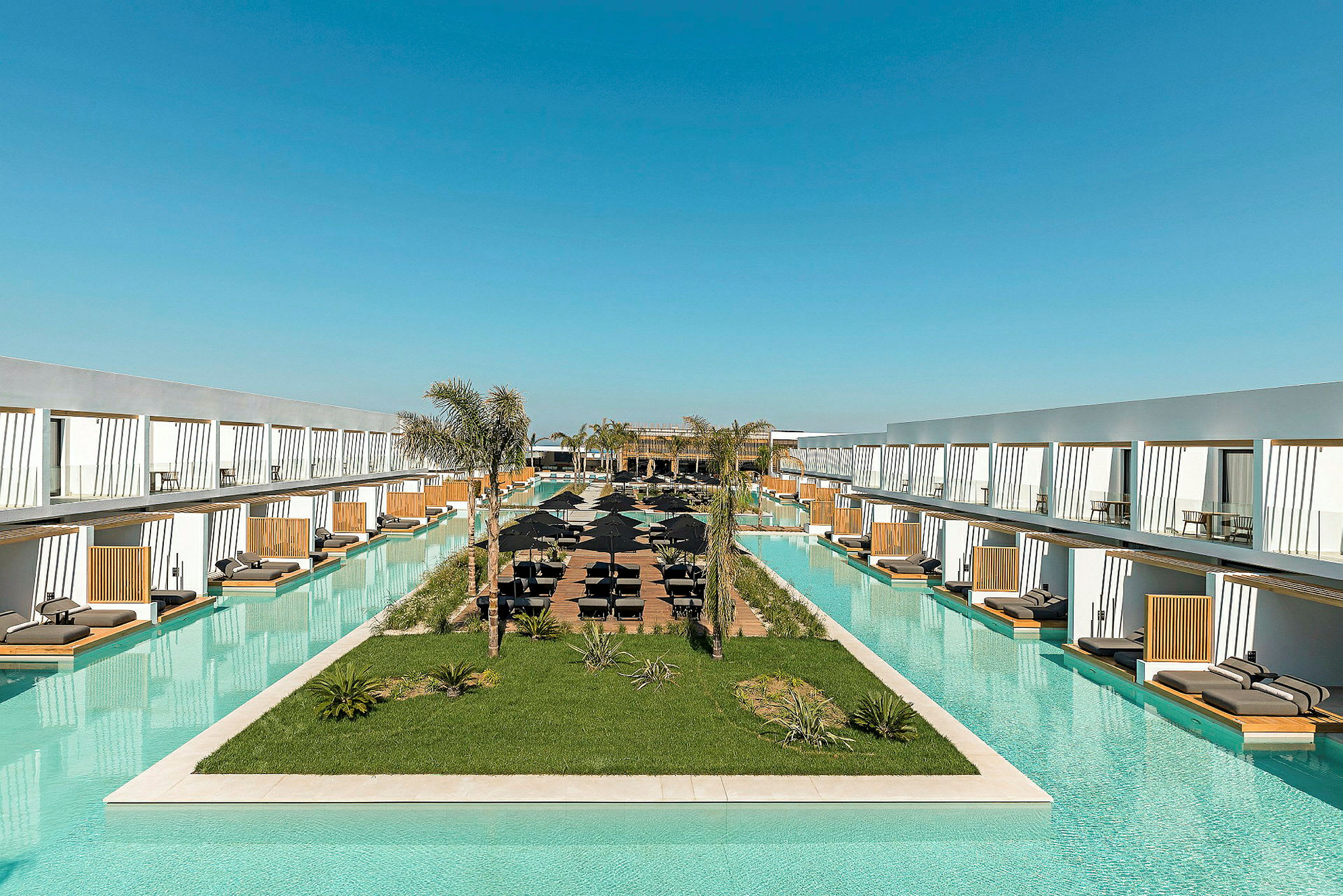 Lång pool omgiven av modernt hotellkomplex med solbäddar. (AI-genererad text)