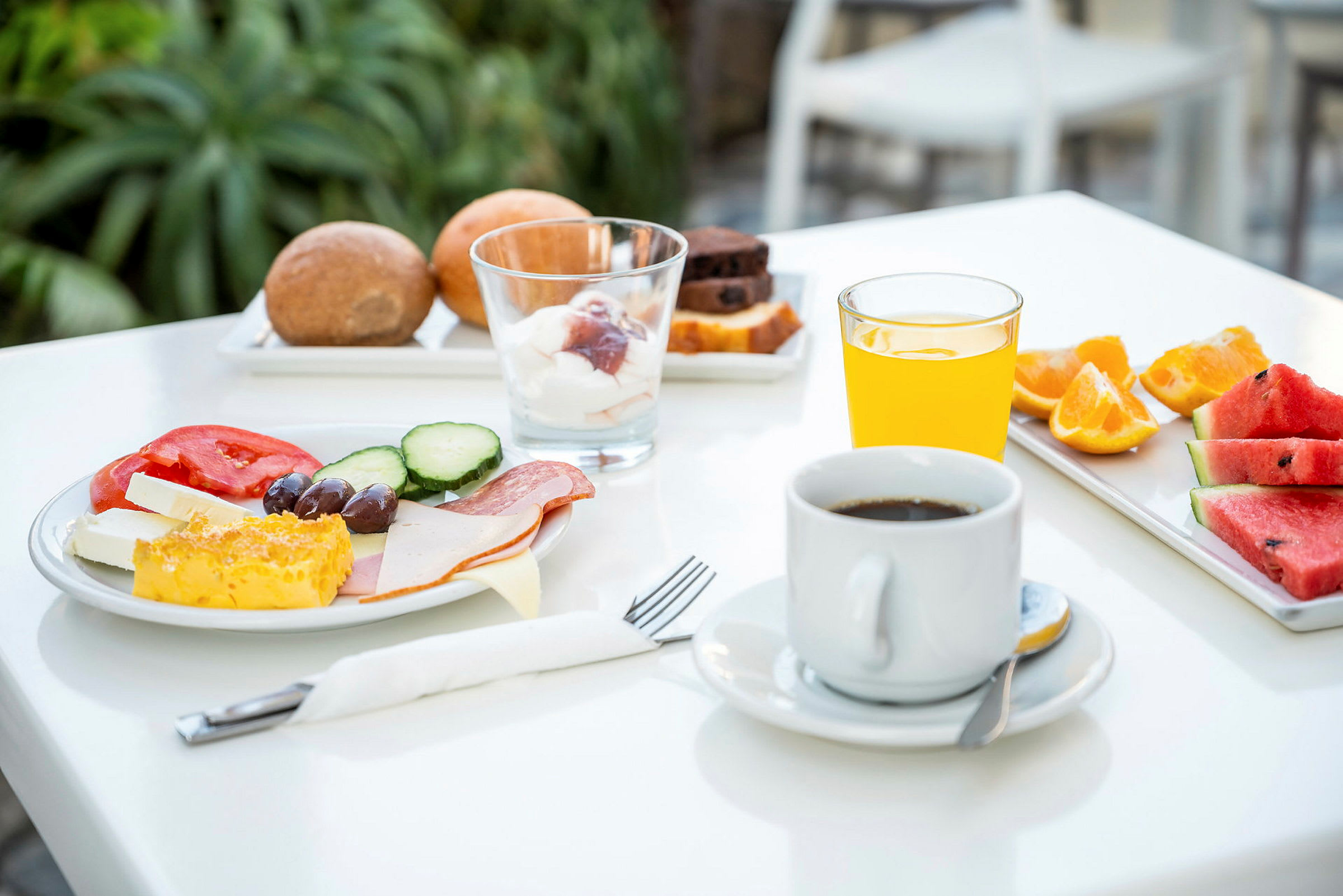 En frukost med kaffe, apelsinjuice, bröd, frukt och grönsaker på ett bord. (AI-genererad text)