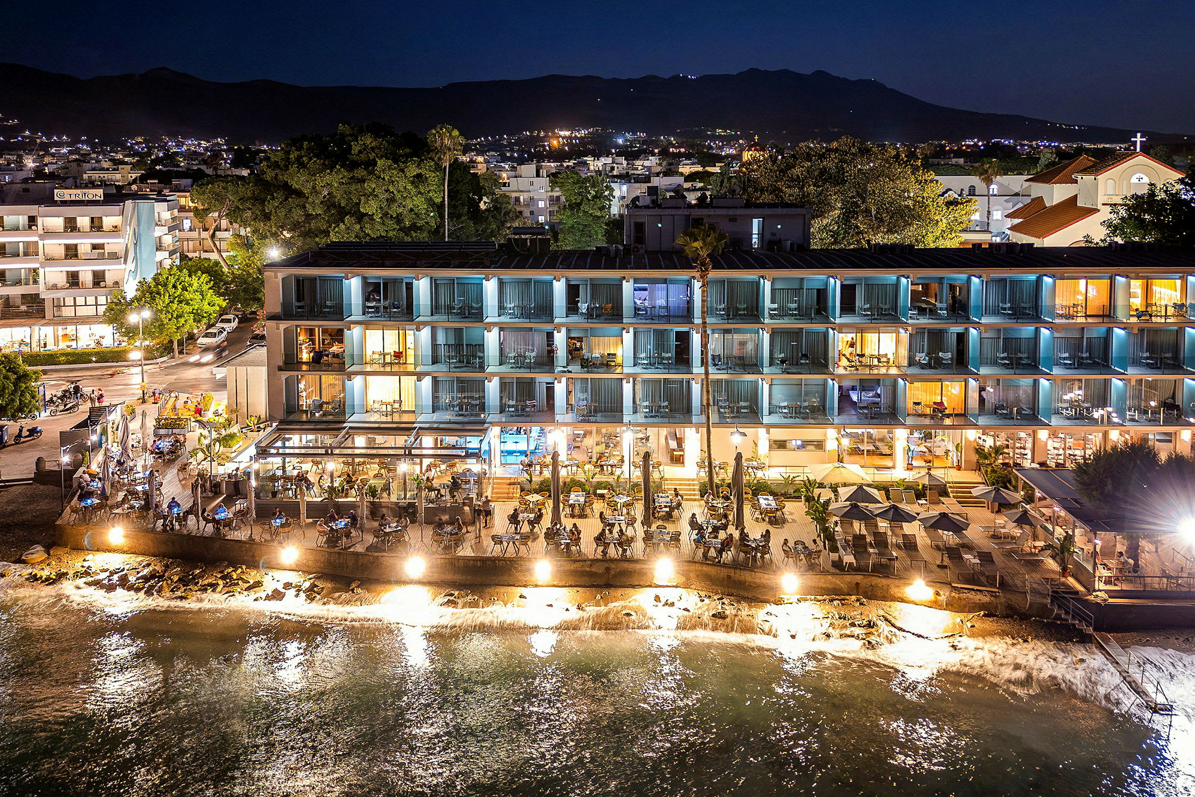 Hotellbyggnad och restaurang vid vattnet, upplyst på kvällen. (AI-genererad text)