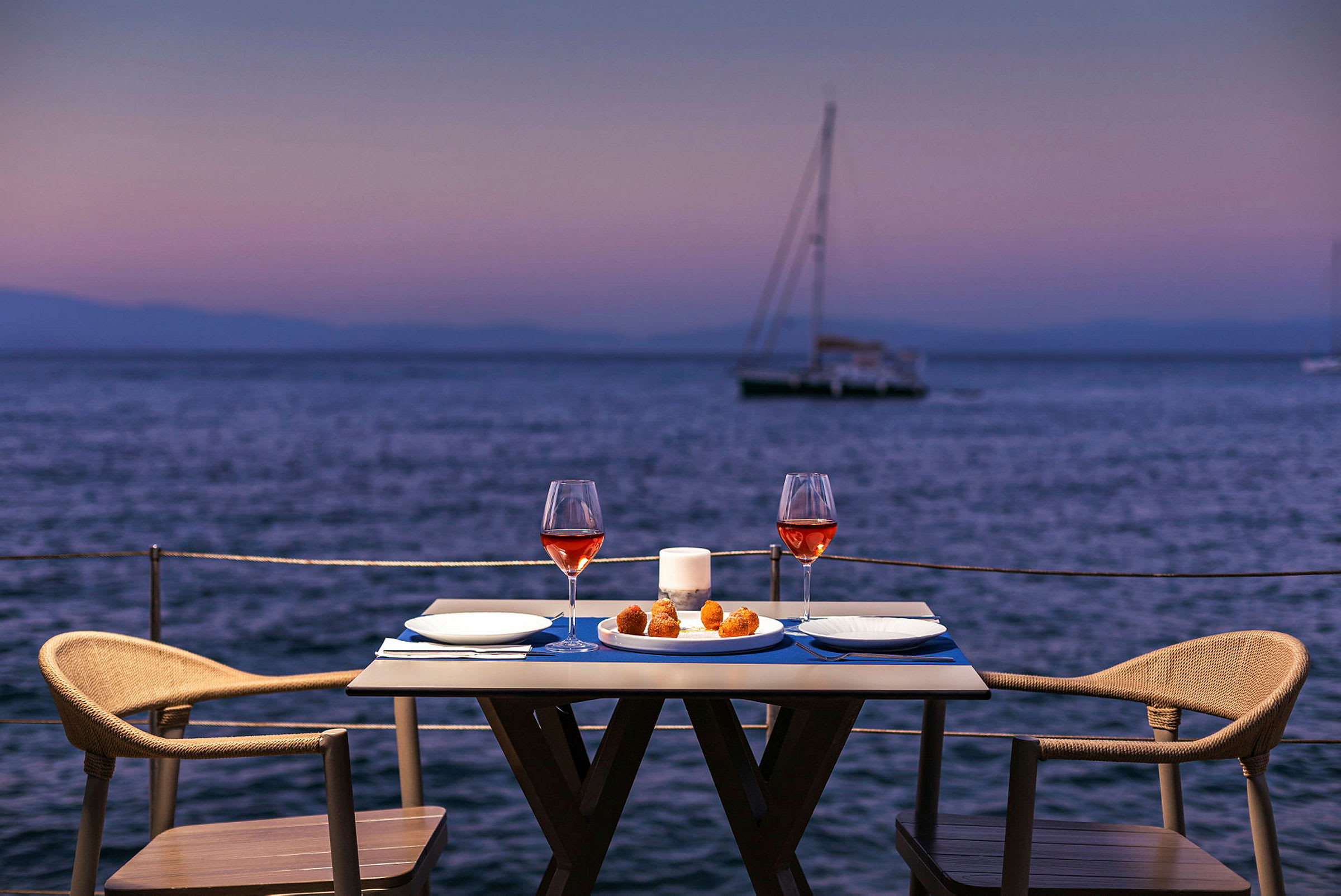 Ett uppdukat bord med vin och mat vid havet i skymningen. (AI-genererad text)