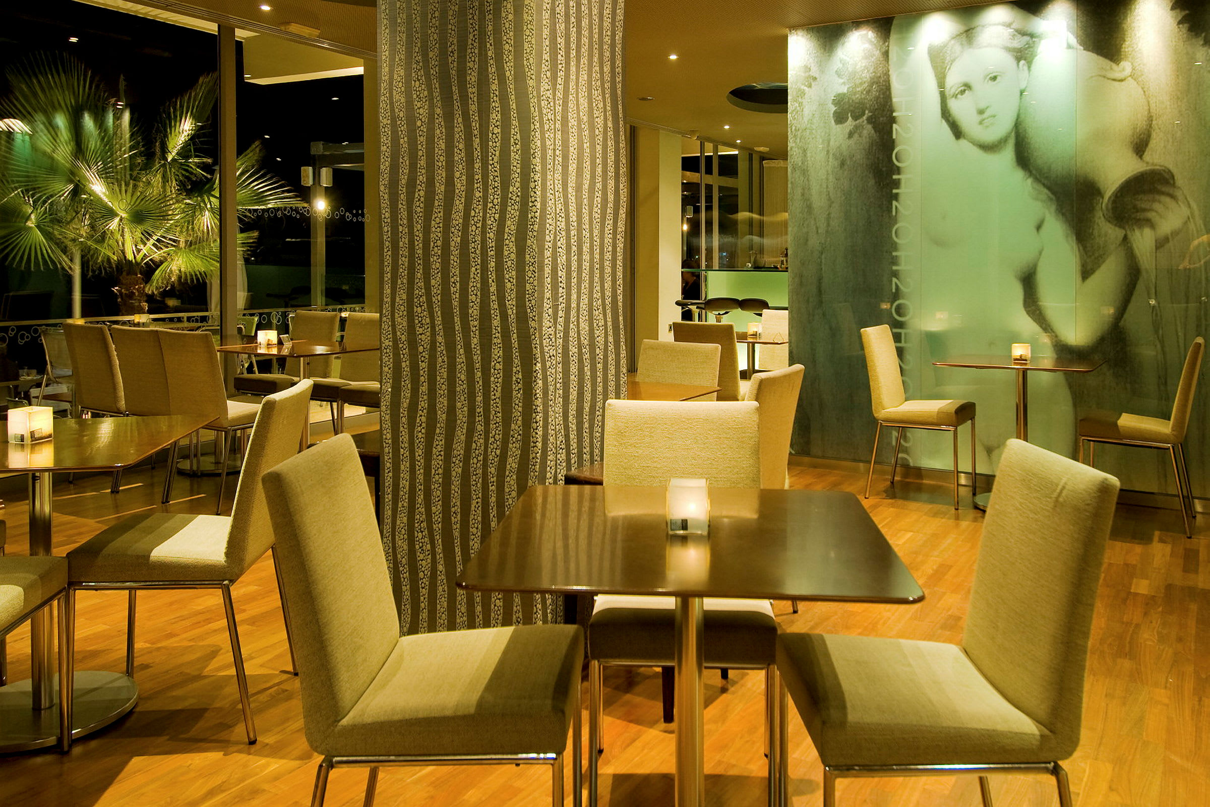 En restauranginteriör med bord och stolar på ett trägolv, omgiven av dekorativa väggar och växter. (AI-genererad text)