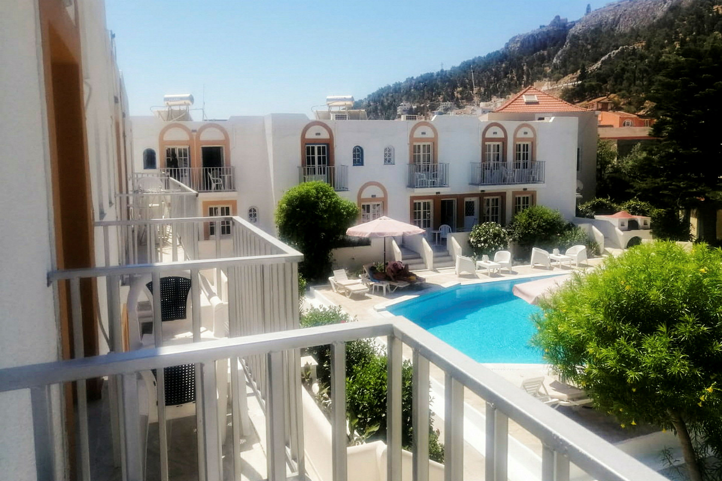 Hotellanläggning med en pool och solstolar omgiven av gröna växter. (AI-genererad text)