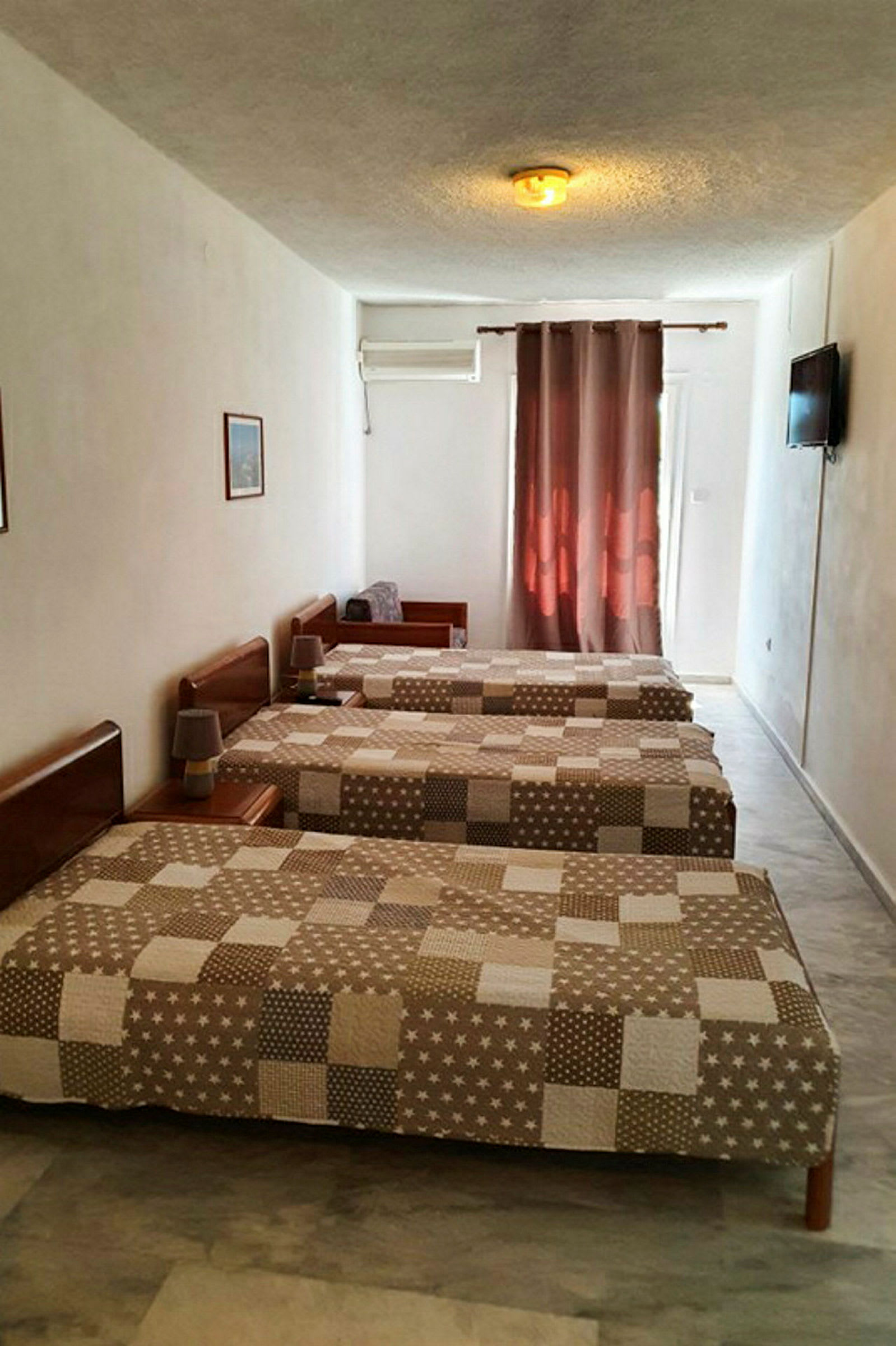 Tre enkelsängar i ett hotellrum med brunmönstrade överkast, luftkonditionering och en TV på väggen. (AI-genererad text)