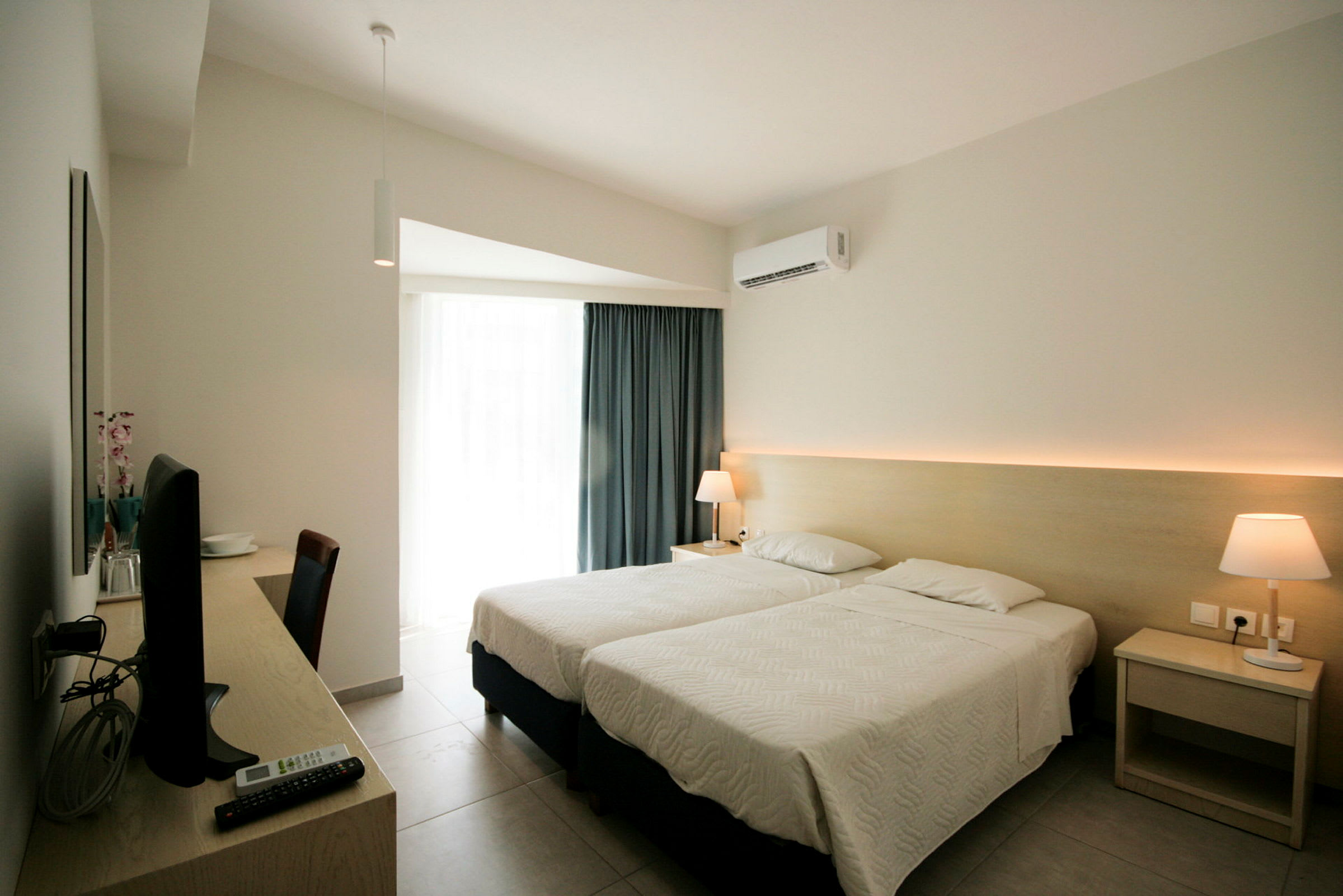 Hotellrum med två enkelsängar, skrivbord med tv och lampa på nattduksbordet. (AI-genererad text)