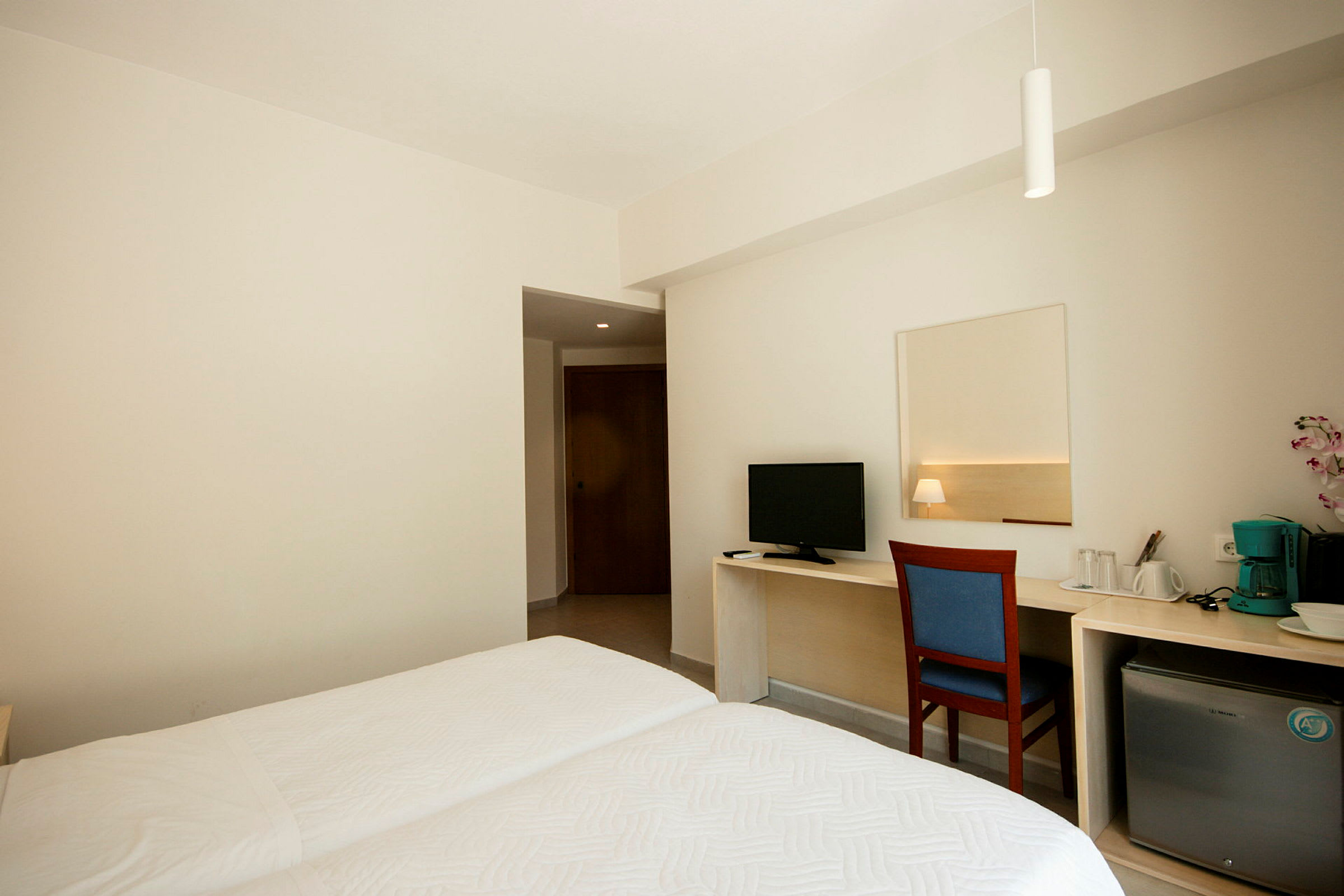 Interiör av ett hotellrum med två enkelsängar, skrivbord med stol, TV, liten kylskåp och kaffemaskin. (AI-genererad text)