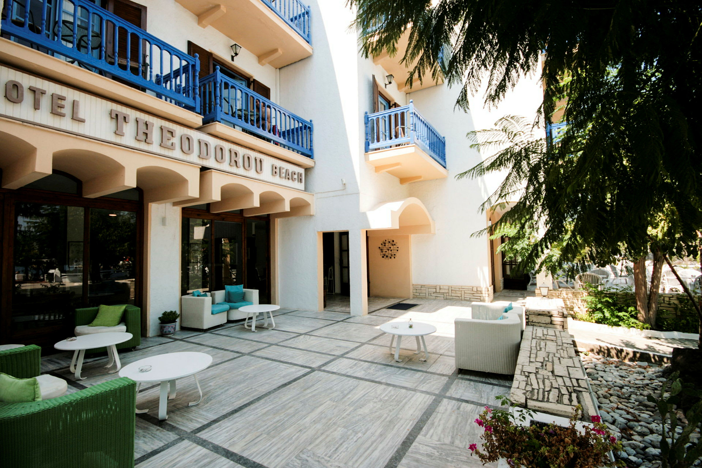 Exteriör av ett hotell med terrass med sittgrupper under blå balkonger. (AI-genererad text)