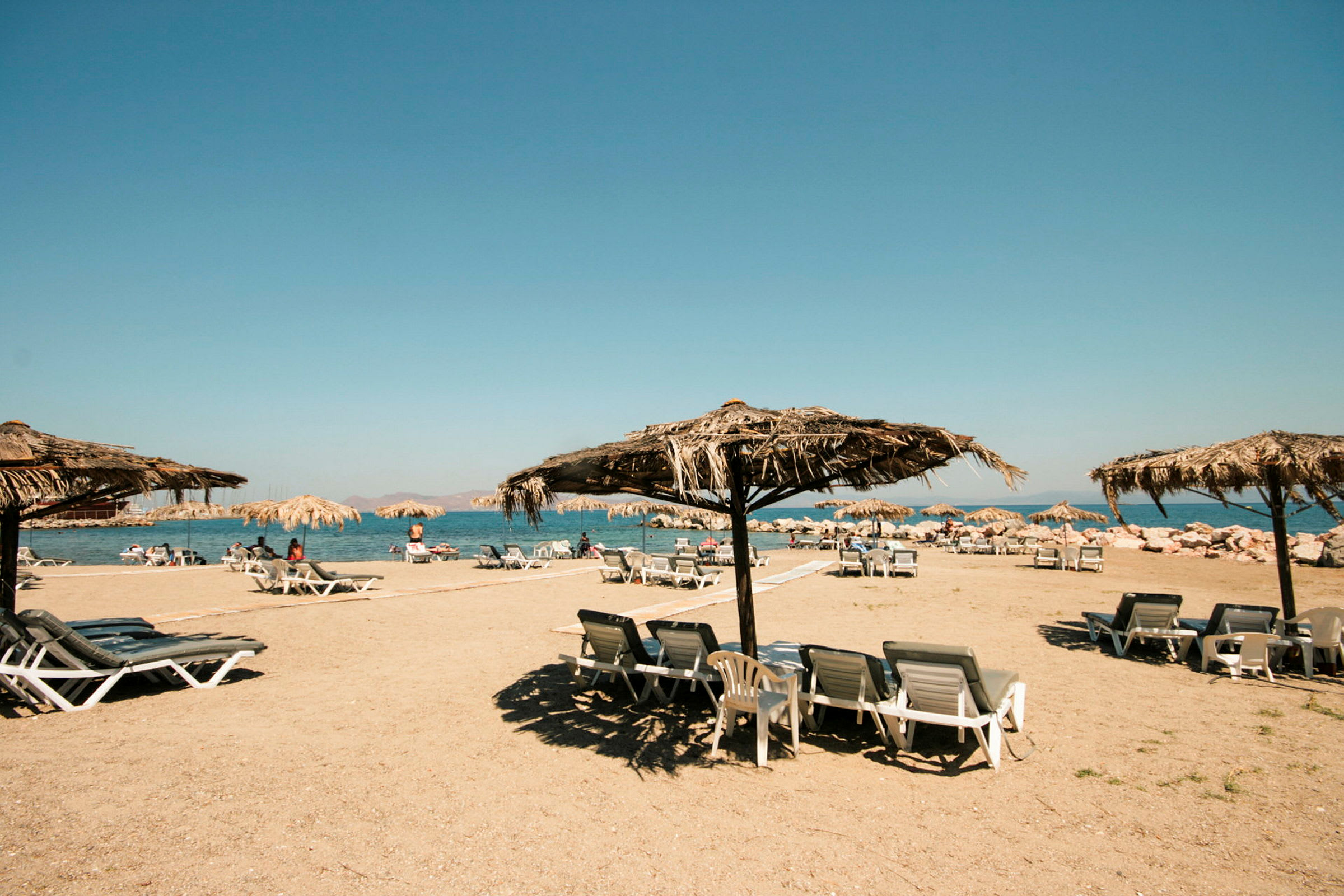 Strand med solstolar och parasoller av halmtak. (AI-genererad text)