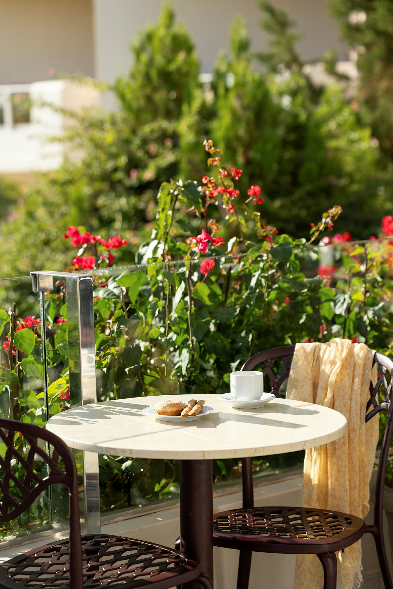Bord med kaffekopp, bakverk och stolar på terrasse med en grönskande omgivning. (AI-genererad text)