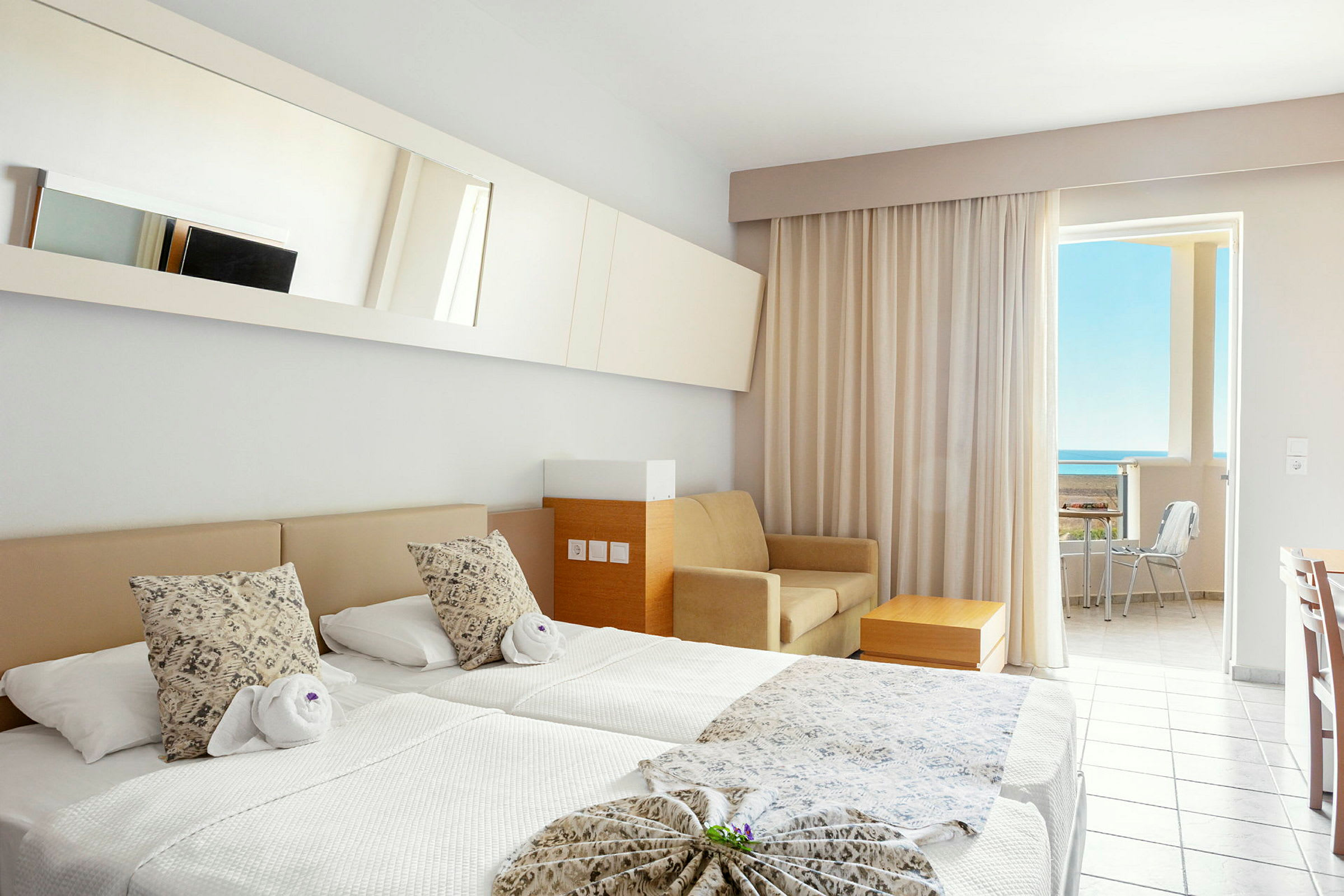Ett hotellrum med två enkelsängar, en soffa, ett bord och en balkong med utsikt mot havet. (AI-genererad text)