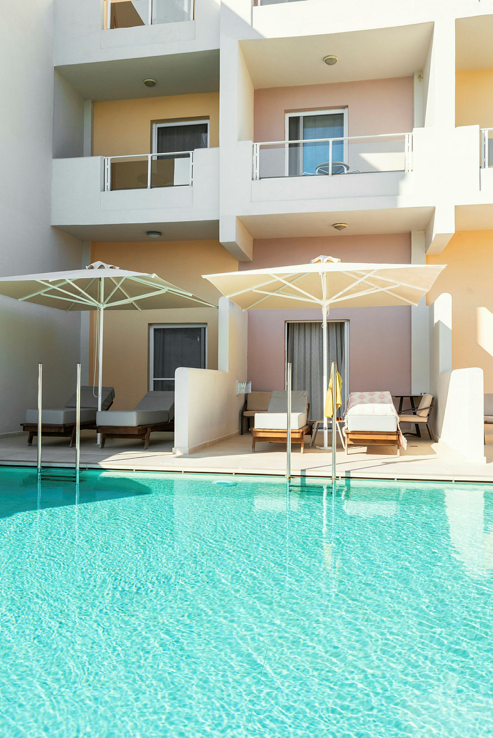 En pool framför lägenhetsbalkonger med solstolar och parasoller. (AI-genererad text)