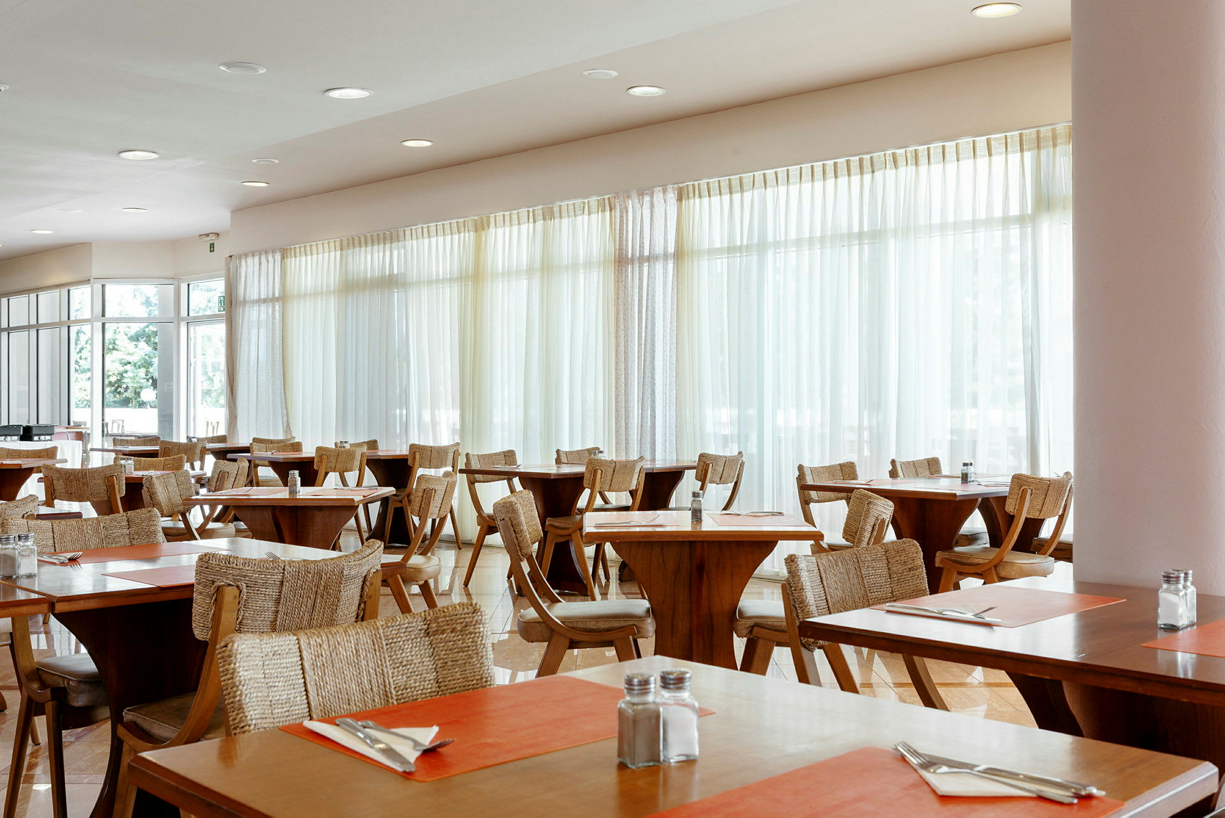 En restaurang med träbord och stolar, dekorerad med orange bordsunderlägg och uppsatt bestick. (AI-genererad text)