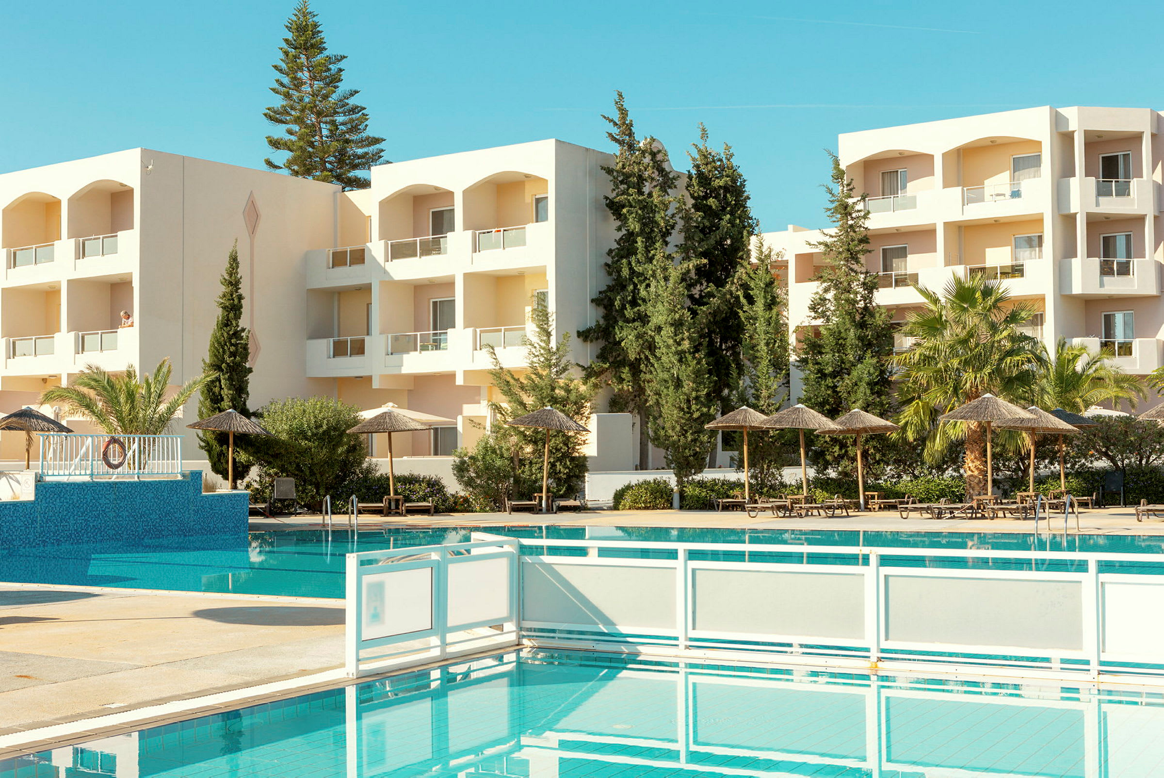 Hotellbyggnad med balkonger, omgiven av grönska och utsikt över en pool. (AI-genererad text)