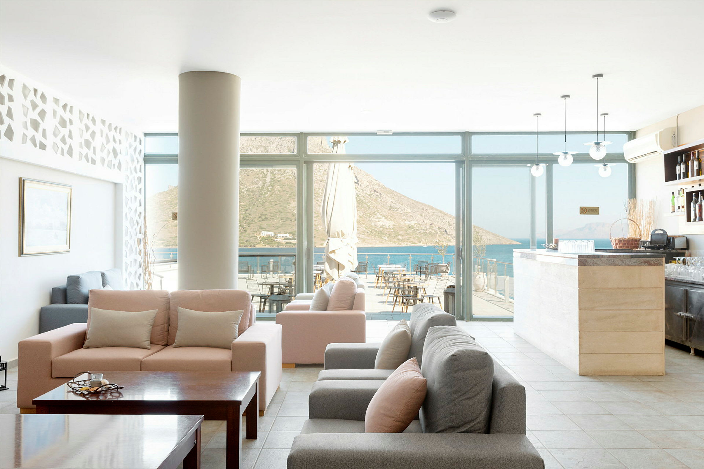 En hotellobby med bekväma soffor, ett bord och glasväggar som visar utsikten mot havet och berg. (AI-genererad text)