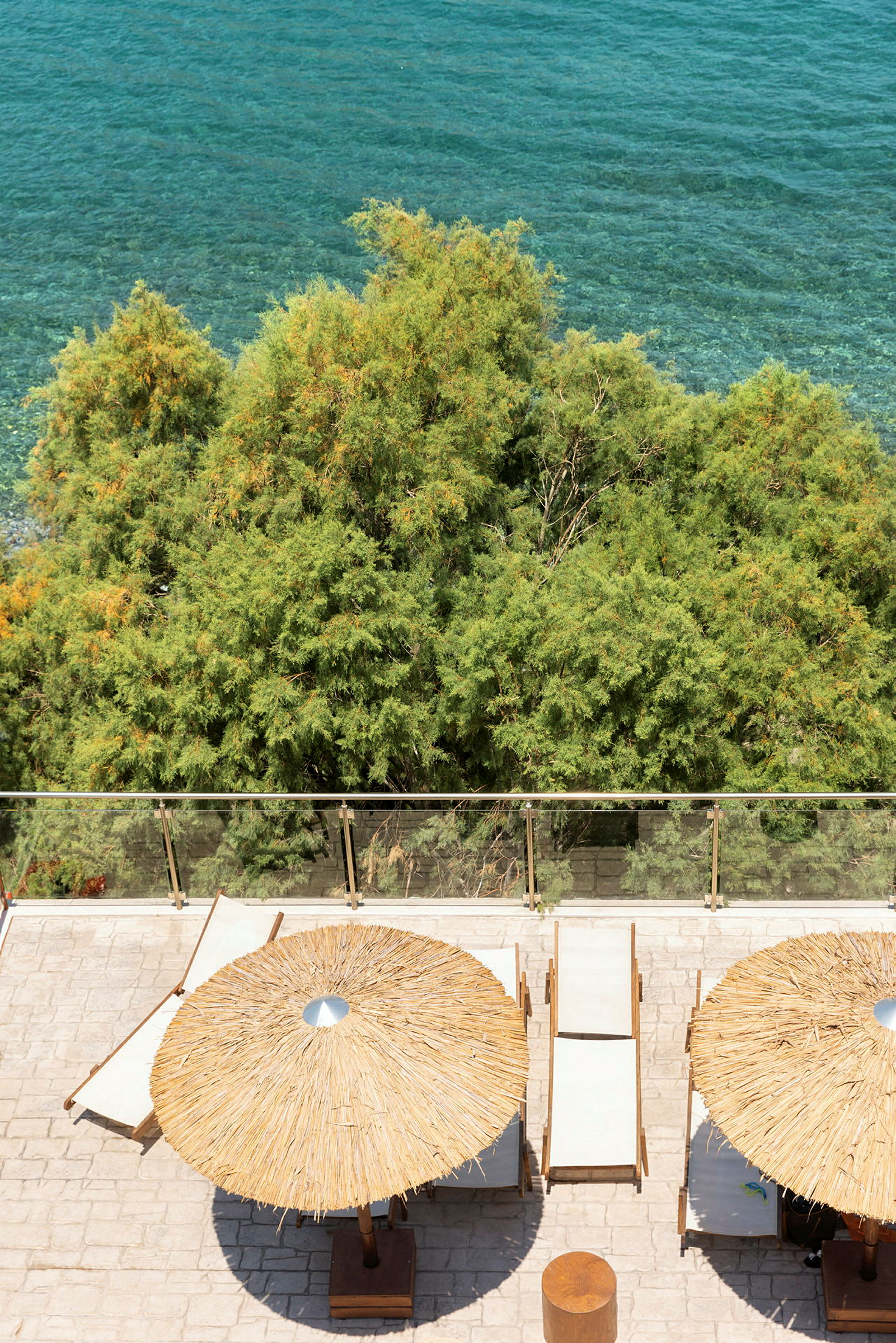 Strandstolar och parasoller vid en terrass med utsikt över havet och gröna träd. (AI-genererad text)