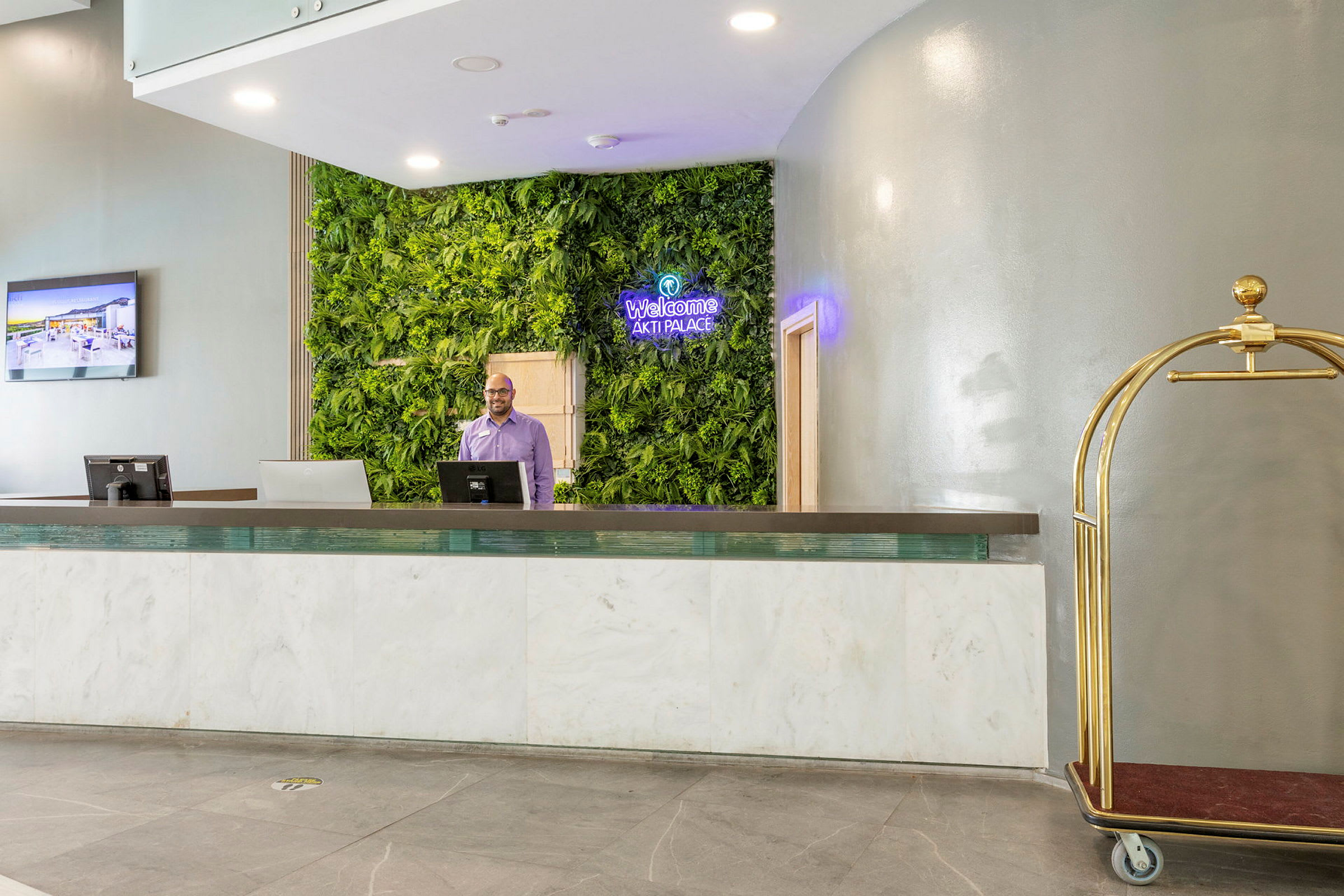 Hotellreception med vägg dekorerad av gröna växter och en bagagevagn. (AI-genererad text)