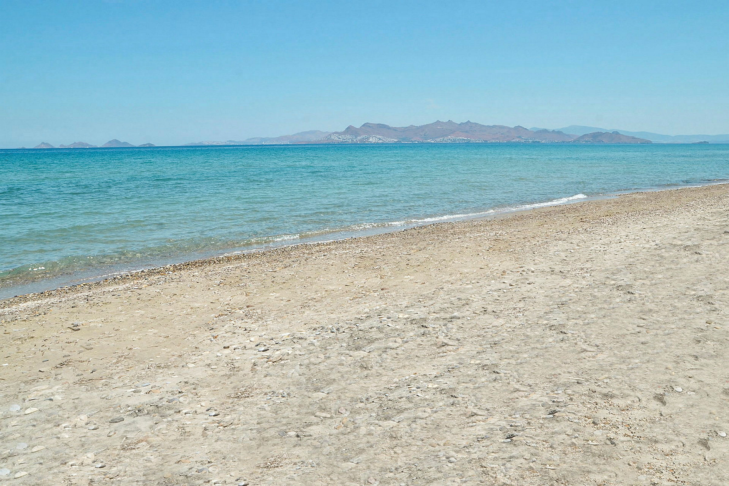 En sandstrand, havet och berg i fjärran. (AI-genererad text)