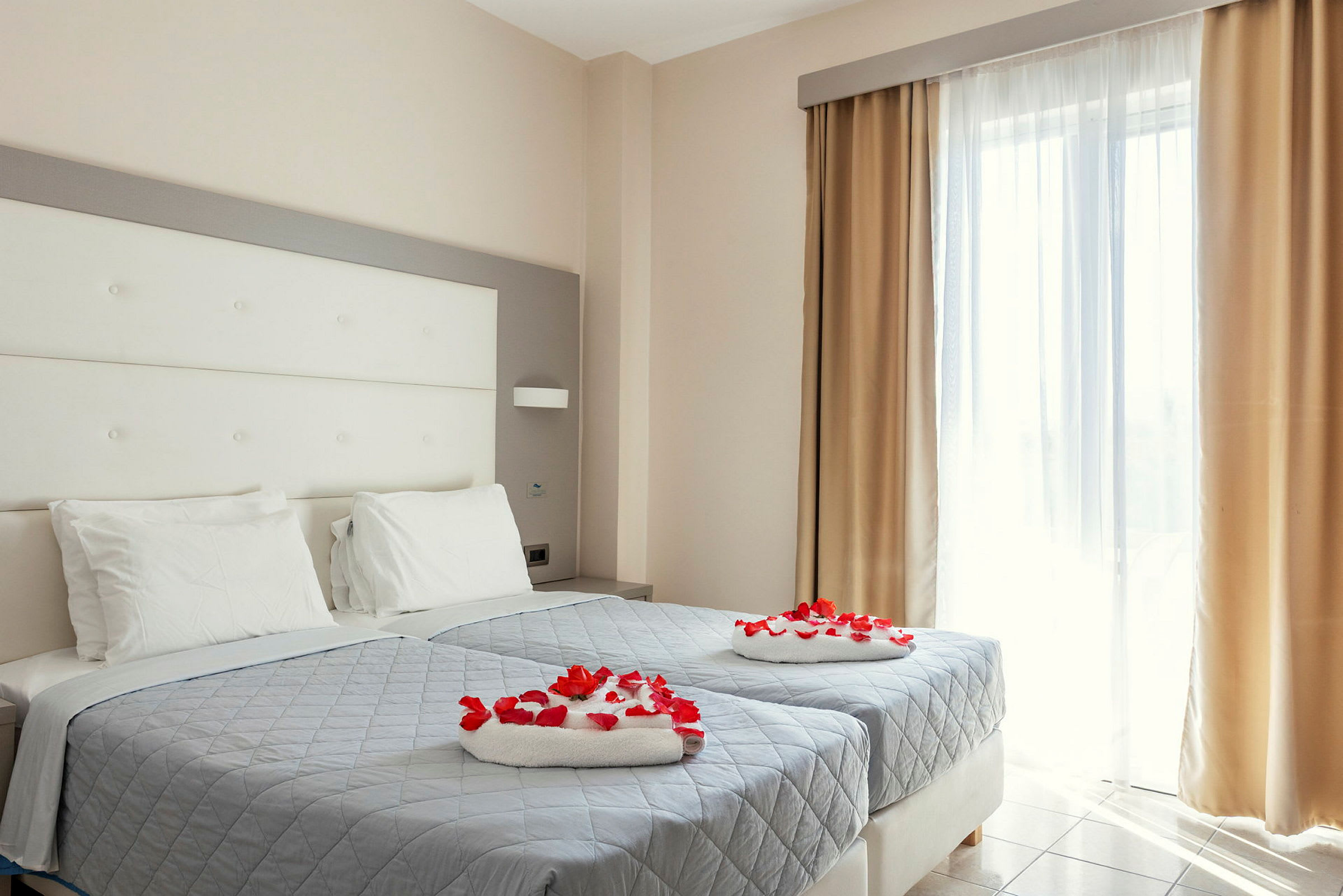 Ett hotellrum med två enkelsängar som är dekorerade med röda rosenblad. (AI-genererad text)