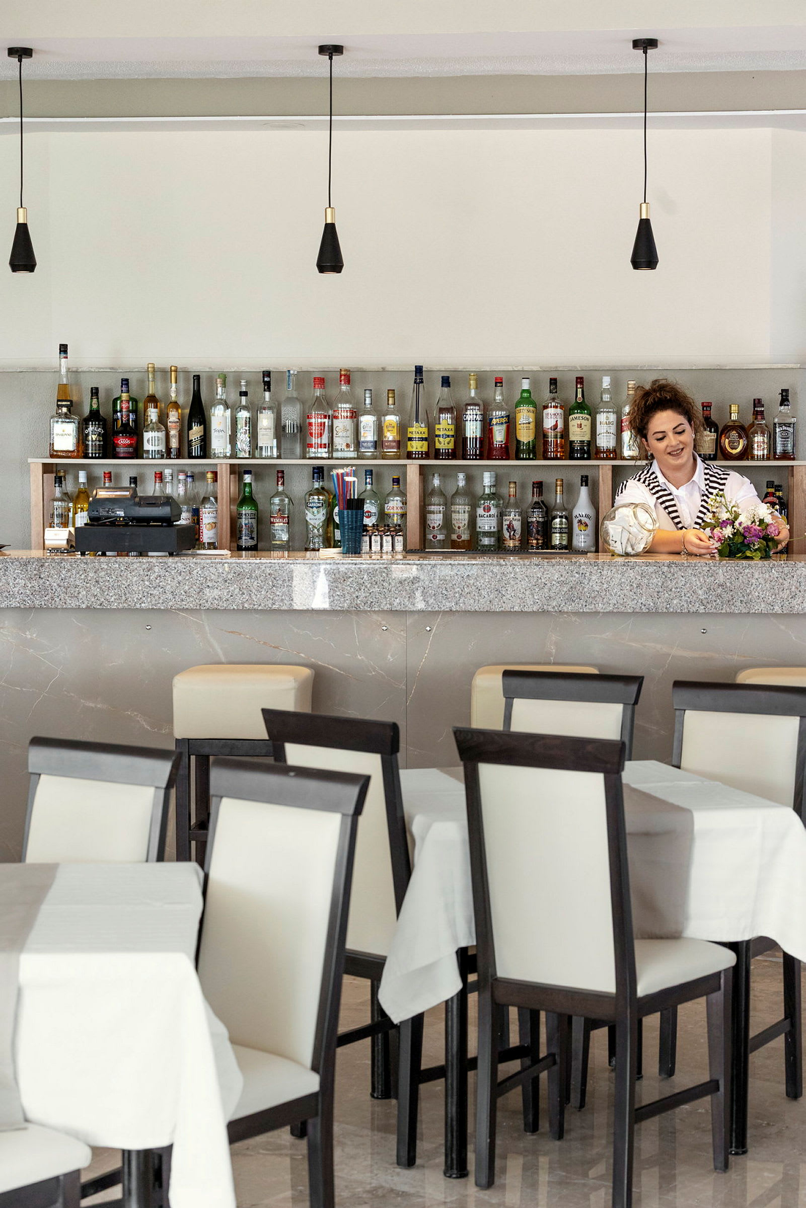 Bar med olika sorters flaskor bakom disken samt bordsplatser framför. (AI-genererad text)