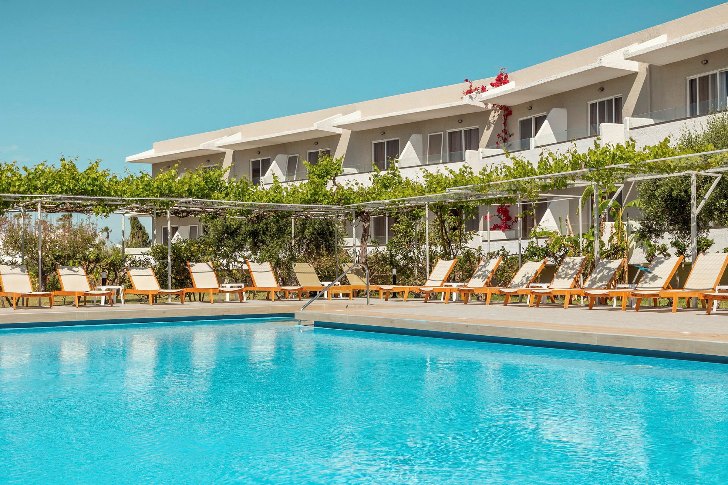 Utomhuspool framför en rad solstolar och ett hotell i bakgrunden. (AI-genererad text)