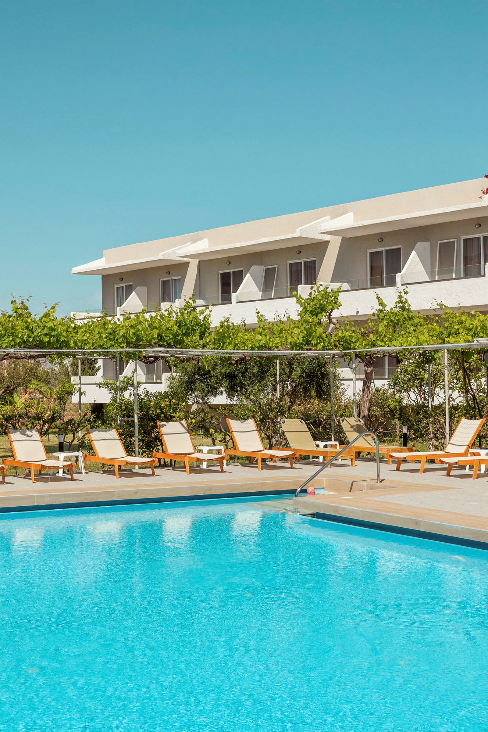 Utomhuspool med solstolar och avkopplingsområde framför ett hotell. (AI-genererad text)