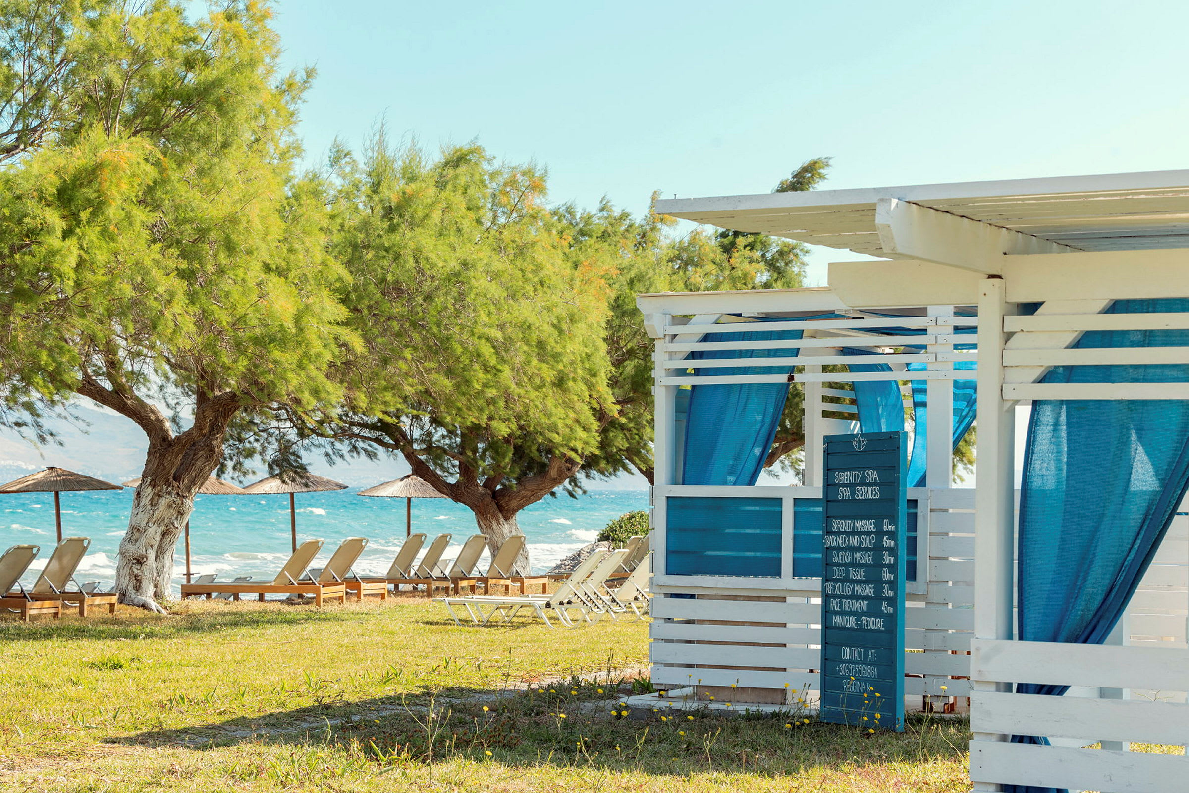 Ett spa med blå gardiner vid en grönskande strand med solsängar och parasoller. (AI-genererad text)