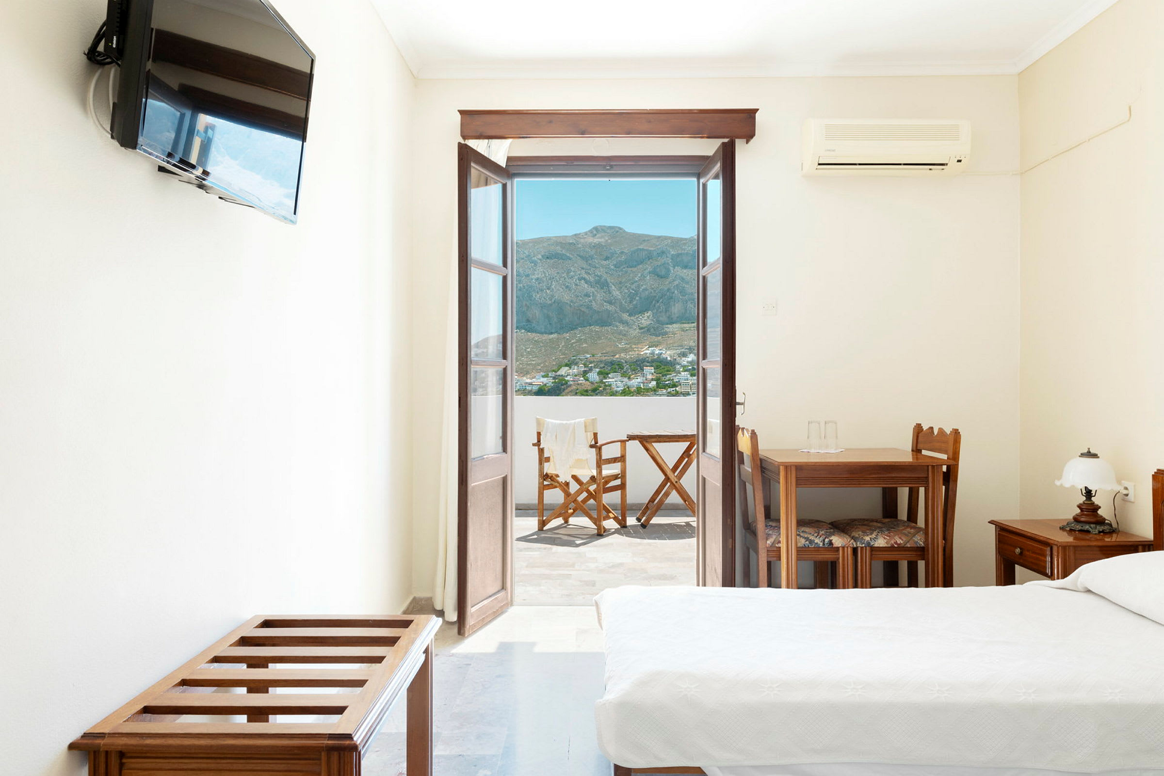 Hotellrum med öppen dörr mot en balkong med utsikt över berg och en by. (AI-genererad text)