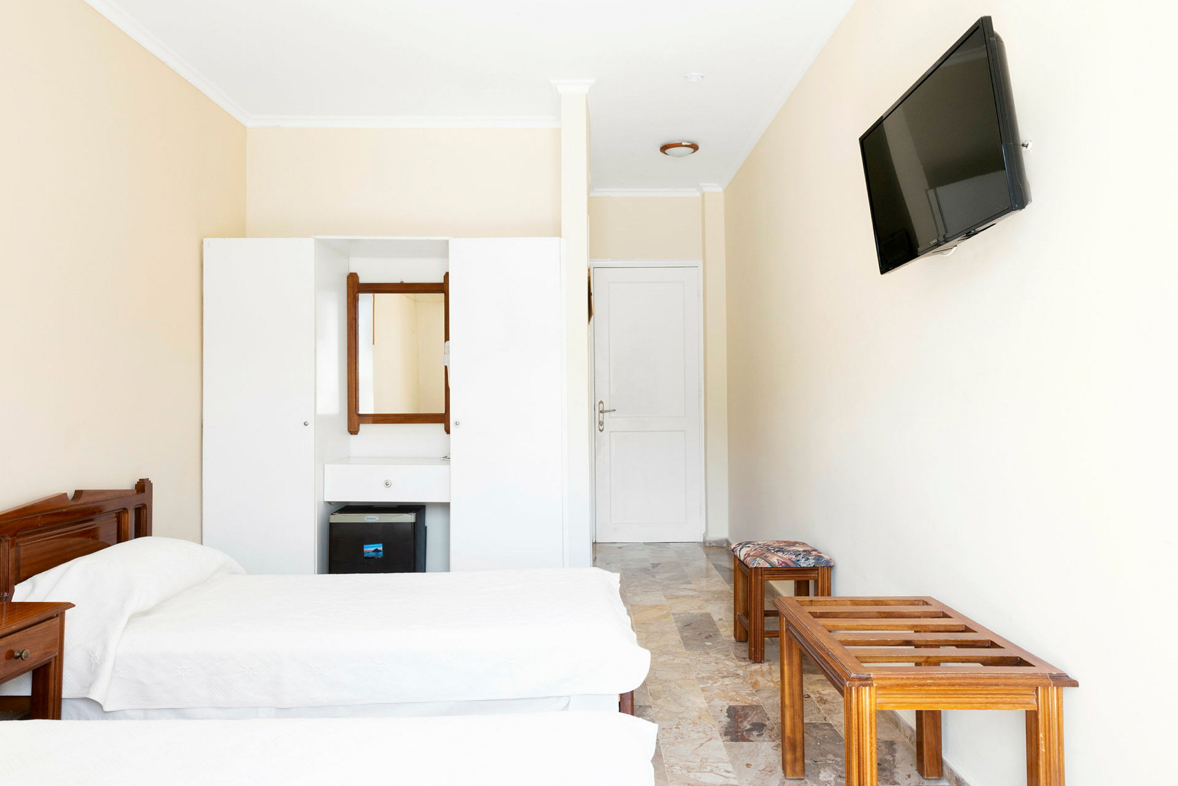 En hotellrumsinteriör med två enkelsängar, en byrå med spegel, och en väggmonterad TV. (AI-genererad text)