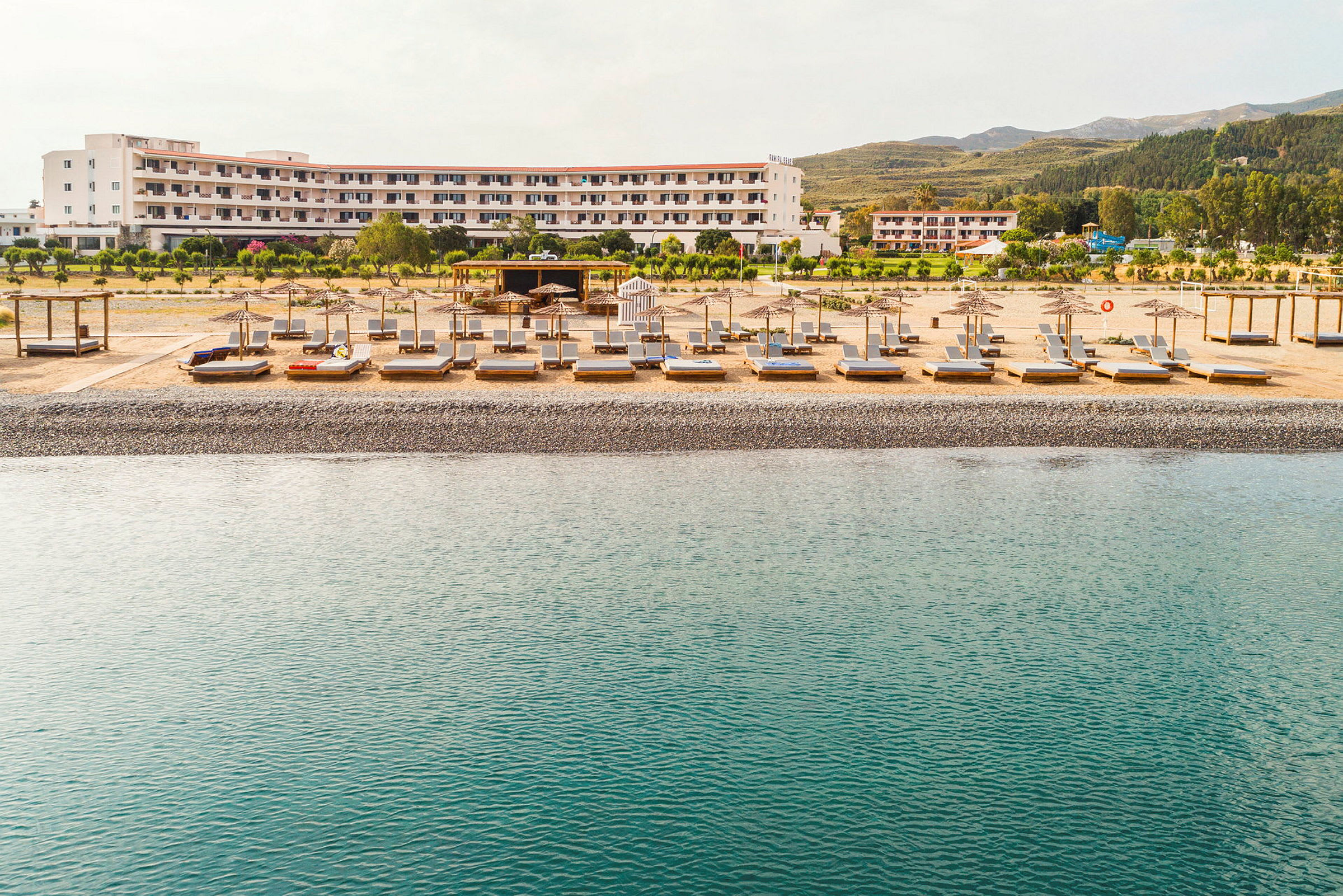 Strand med solstolar och parasoller framför ett hotell. (AI-genererad text)