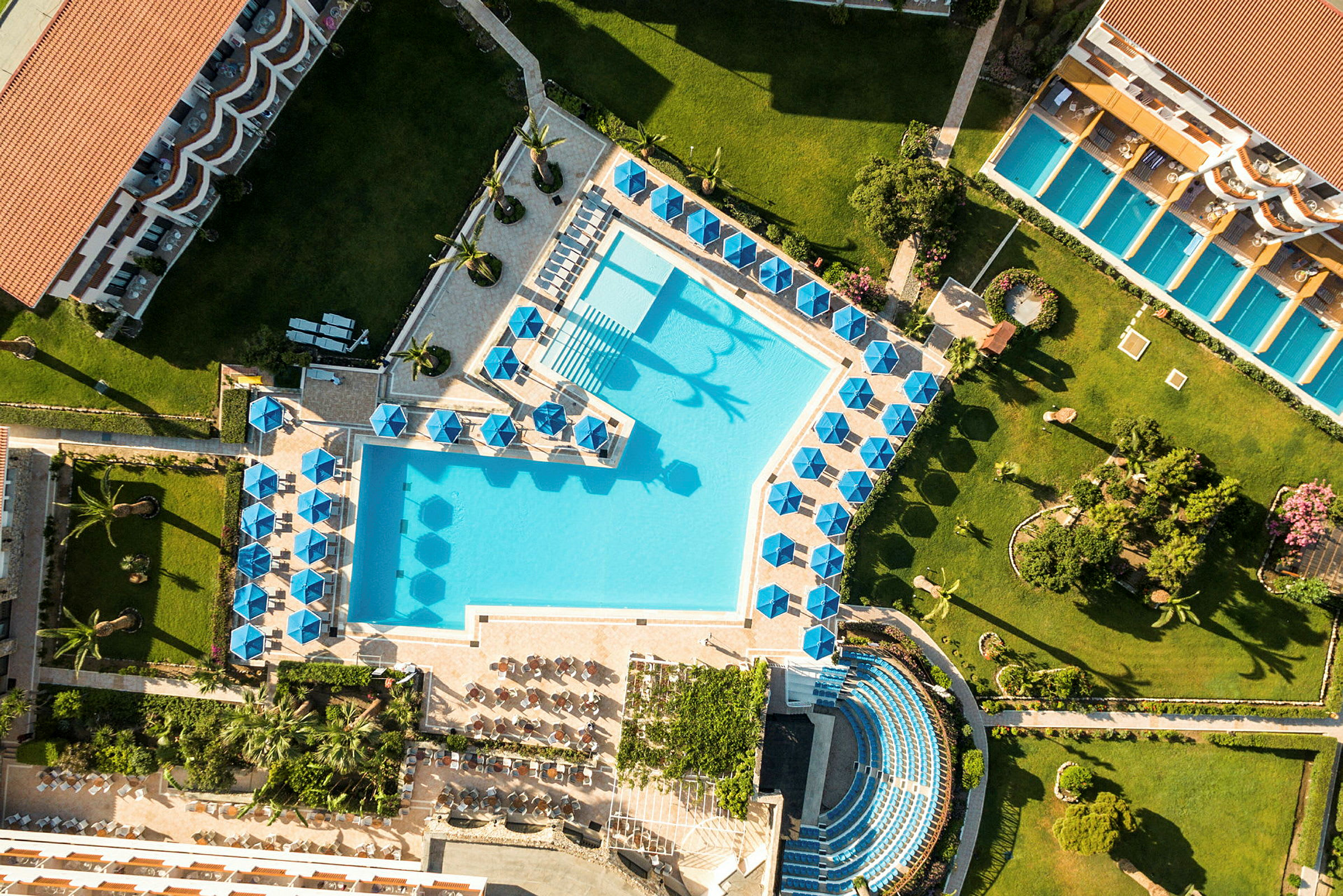 Flygbild av ett hotellområde med pool, solstolar och grönska. (AI-genererad text)
