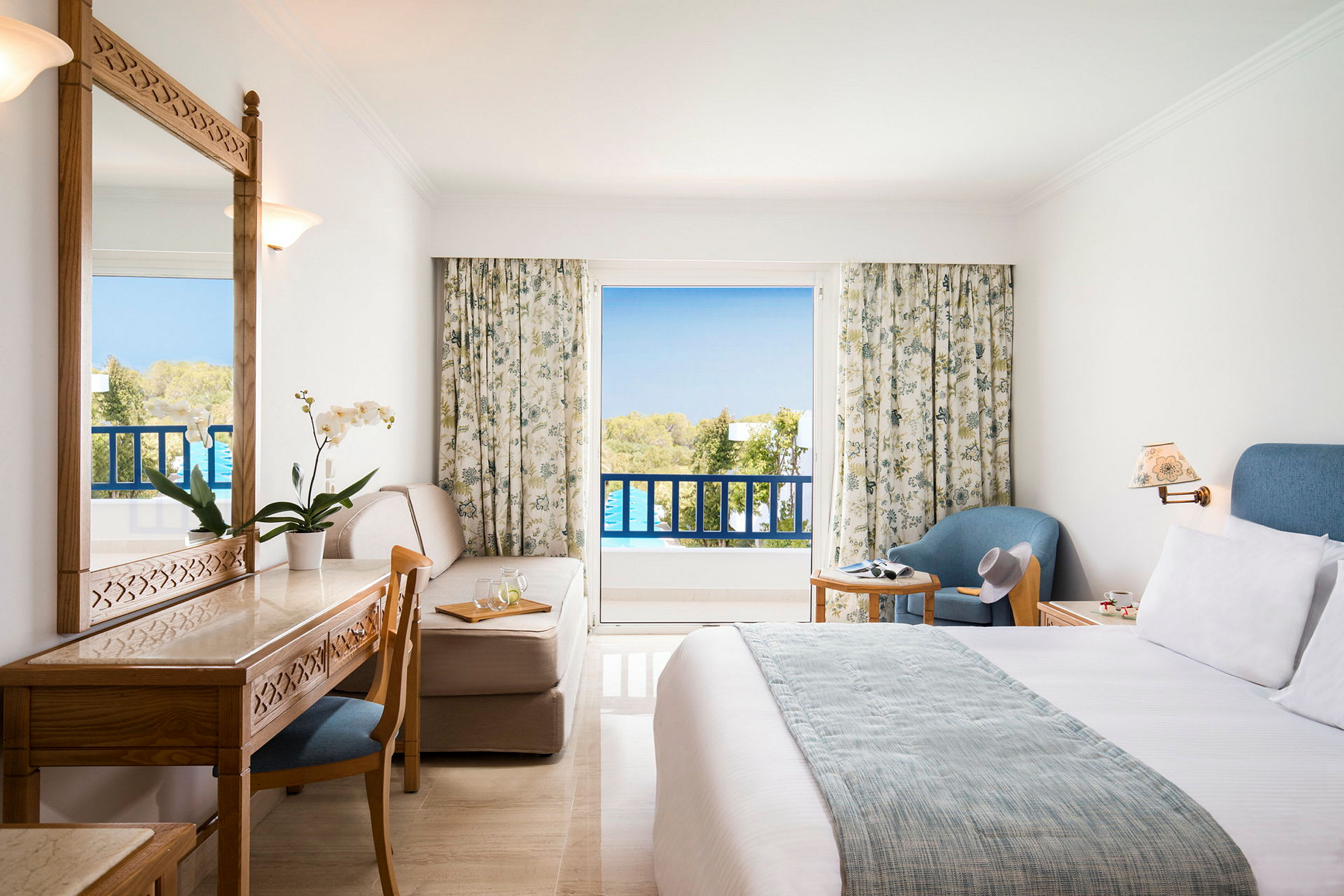Ett hotellrum med balkong, möbler inklusive säng, skrivbord, stol och fåtölj. (AI-genererad text)