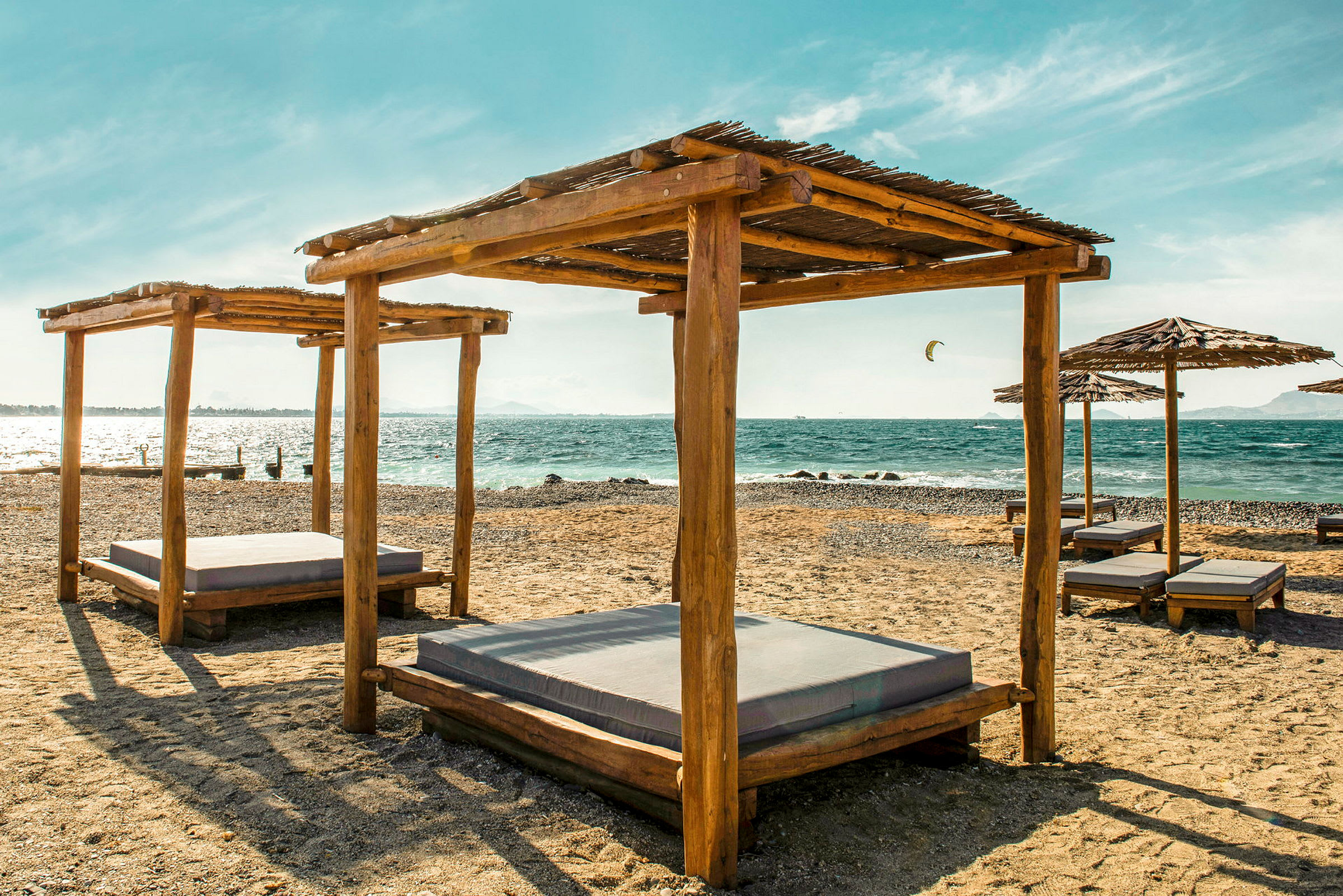Solstolar med träskydd på en sandstrand vid havet. (AI-genererad text)