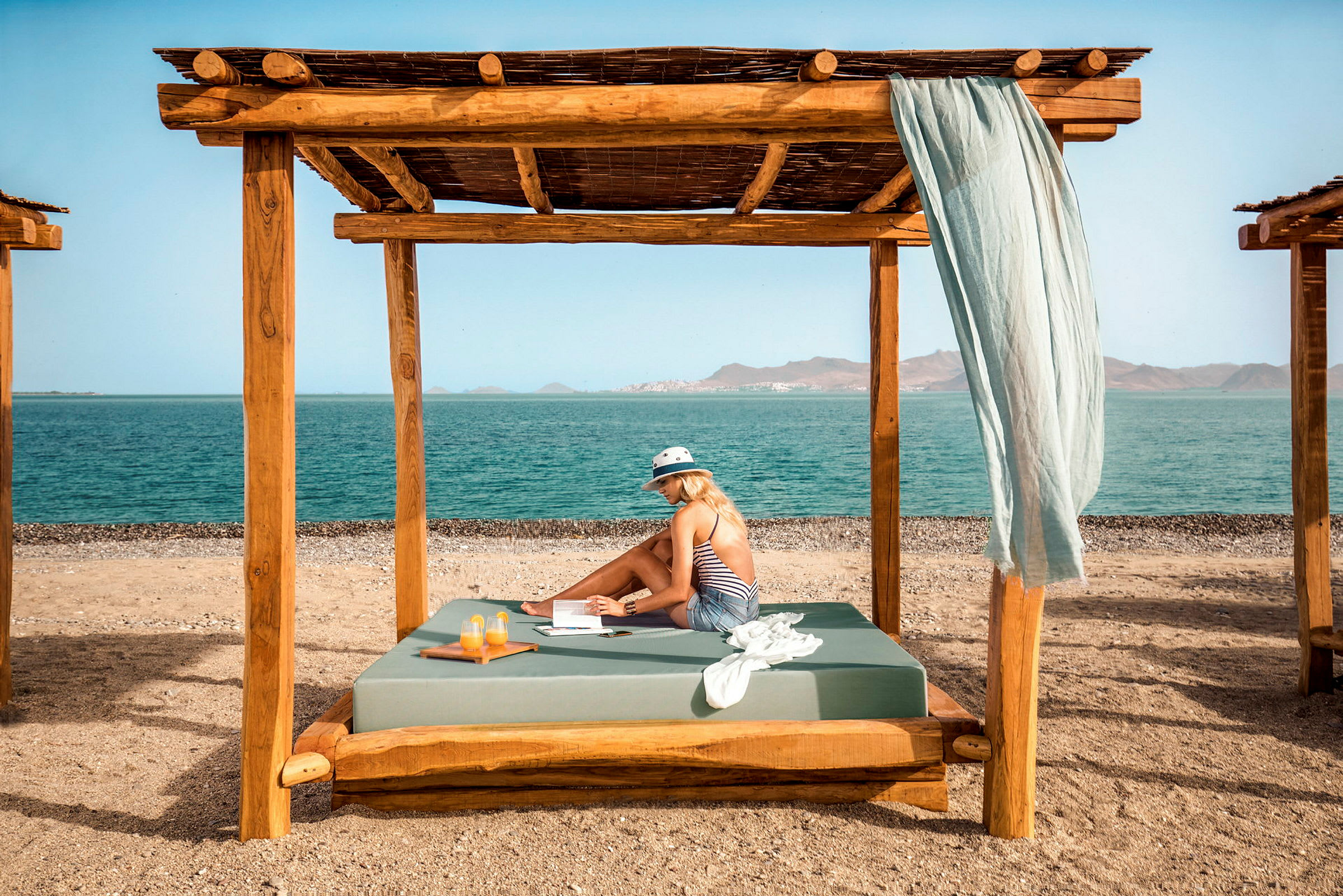 En person sitter under en träpergola på en strand med havet i bakgrunden. (AI-genererad text)