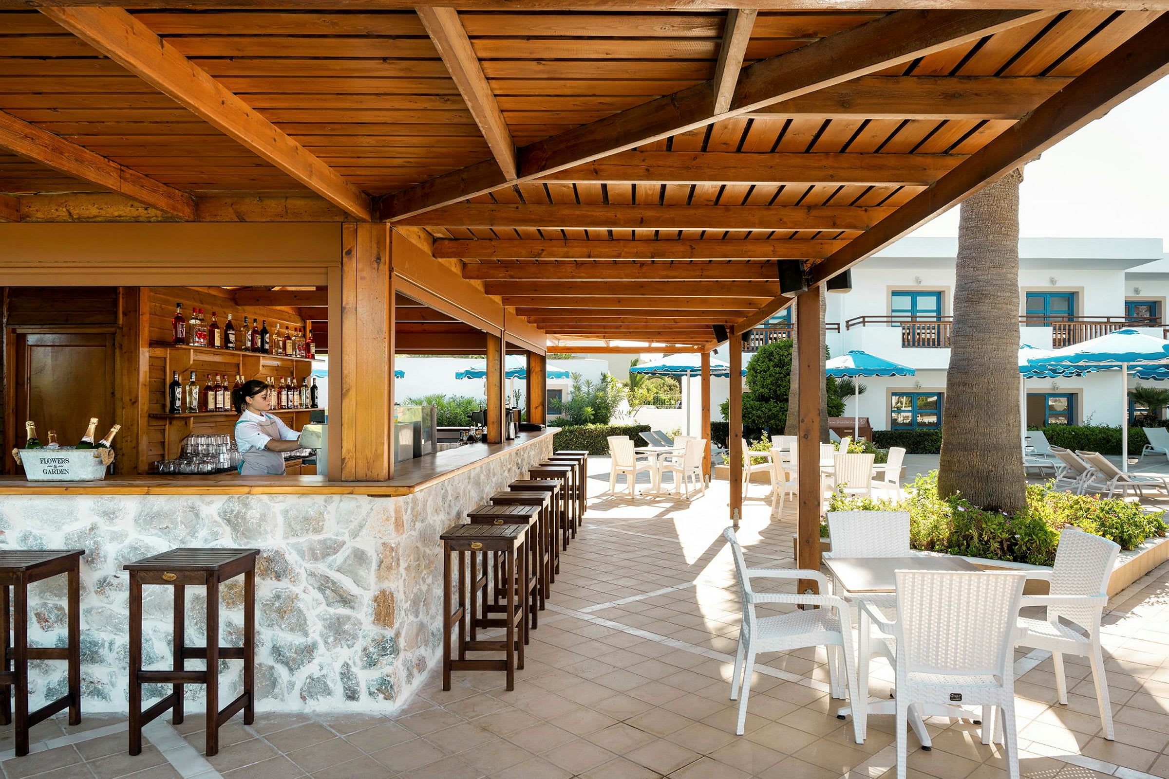 Bild av ett utomhusområde med en bar under ett trätak, stolar och bord i en terrassmiljö. (AI-genererad text)